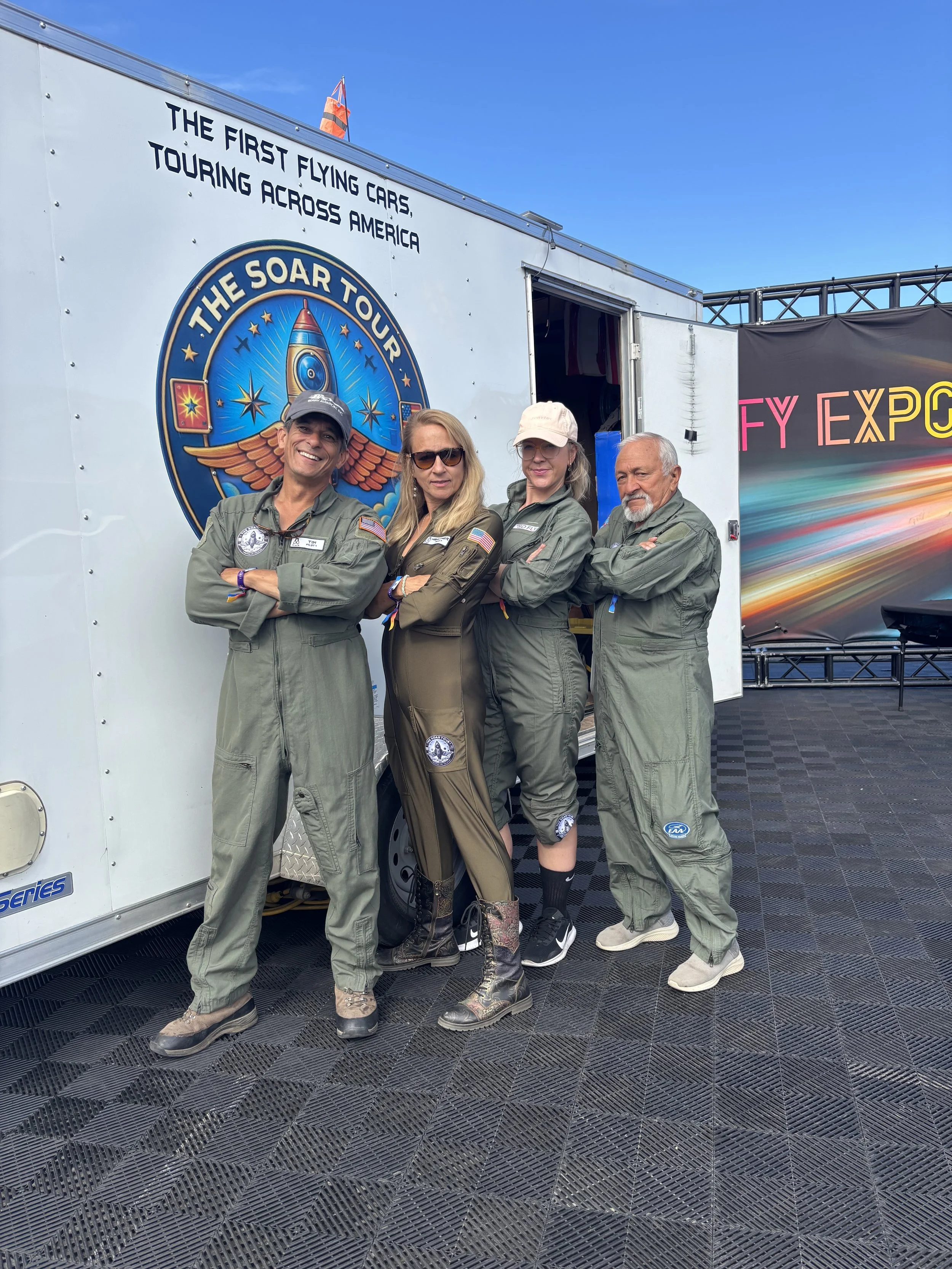 Heather Chirtea's team dressed in aviation jumpsuits standing with arms crossed in front of a trailer with NASA and space-themed logos at an airshow or expo.