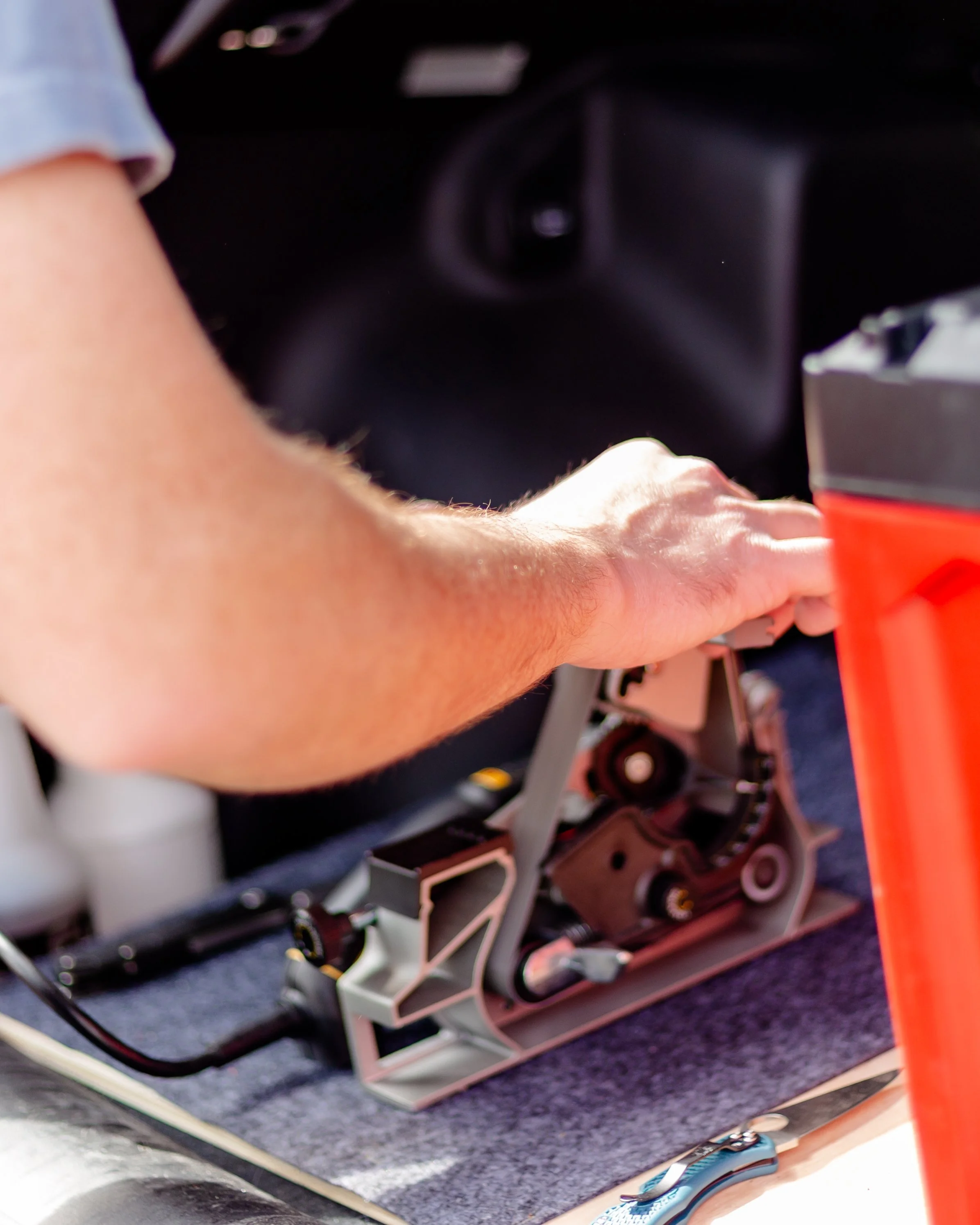 Close-up of a person's arm  sharpening a knife on a small belt grinder on a work surface set up in the trunk of a vehicle.