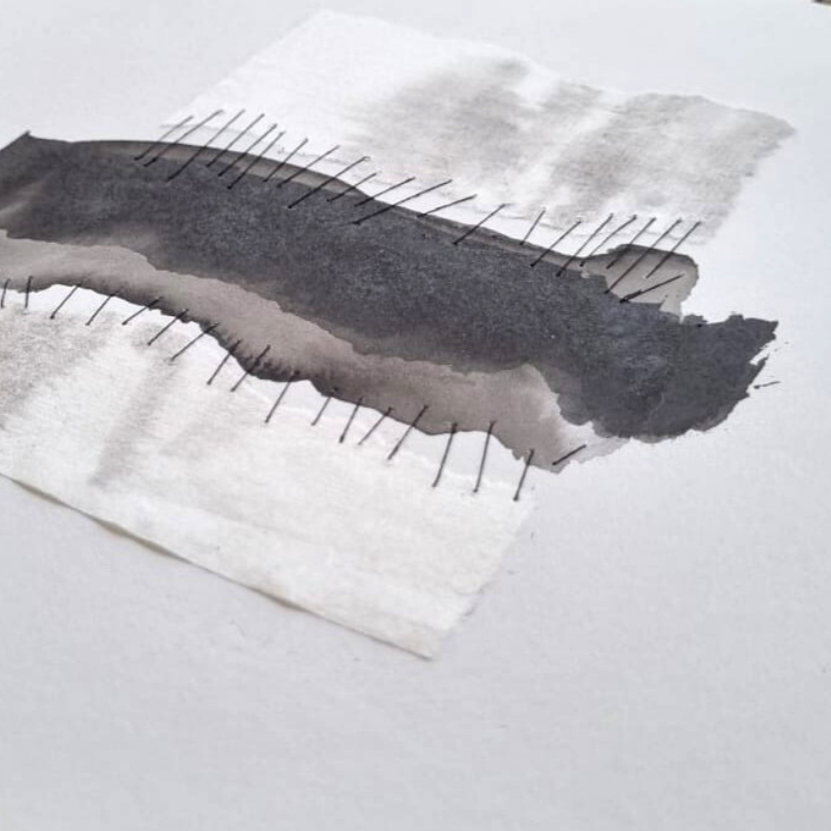 Trazado de tinta negra en papel con varias agujas de coser atravesándolo, creando patrón abstracto.