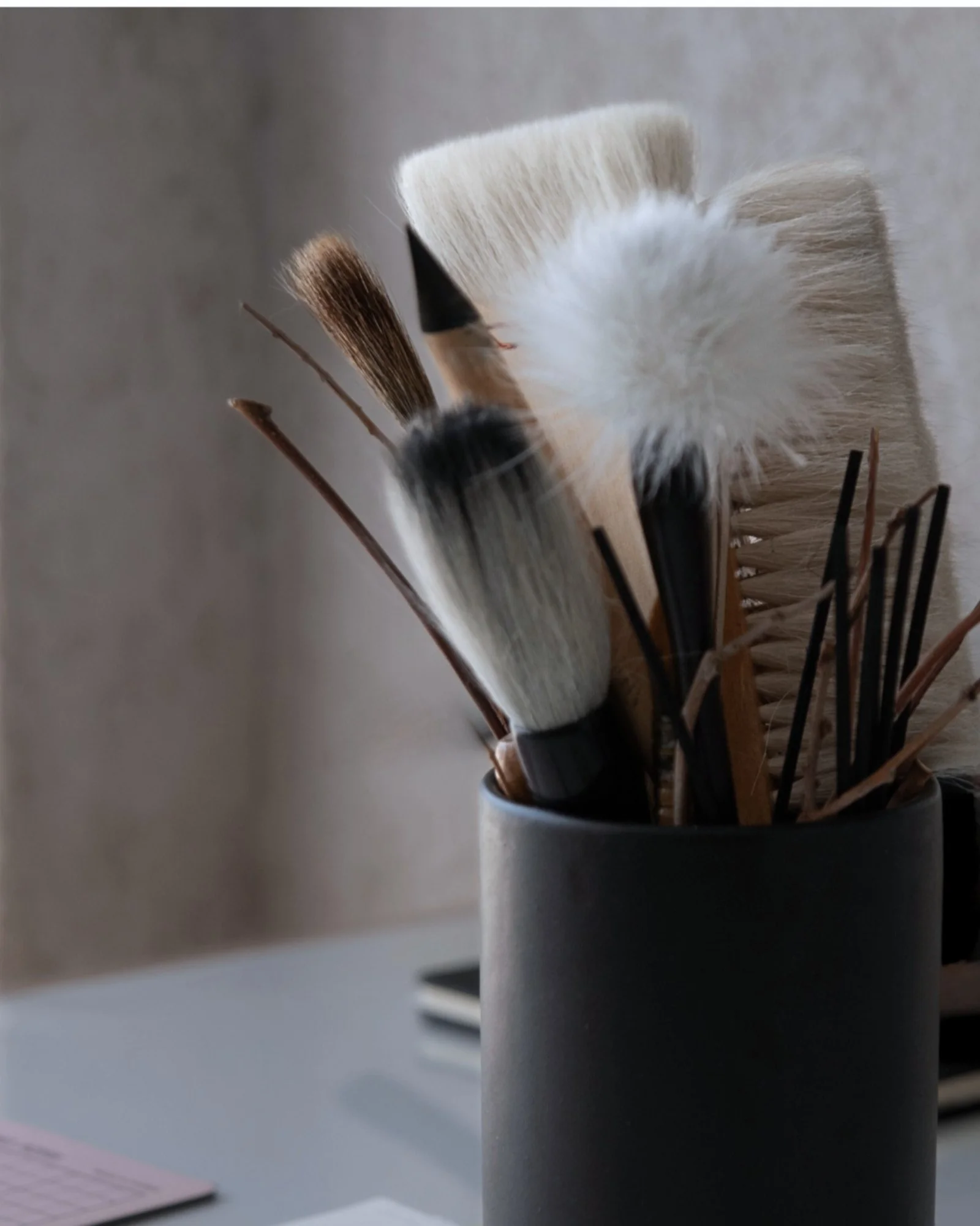 Pinceles y herramientas de artista en un recipiente negro dentro de un espacio de trabajo.