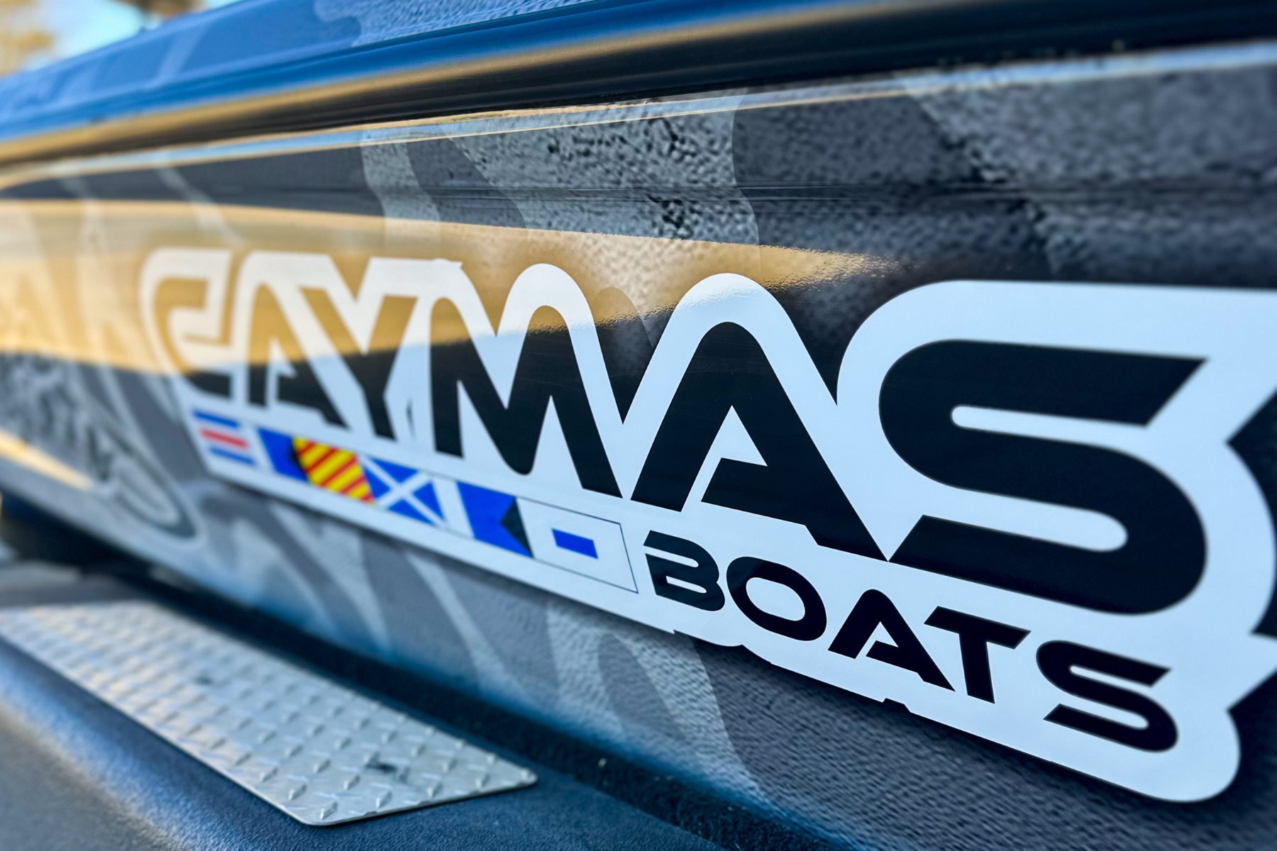 Close-up of a sticker on a boat with the text 'MAX BOATS' and a small flag with red and yellow stripes and blue crosses.