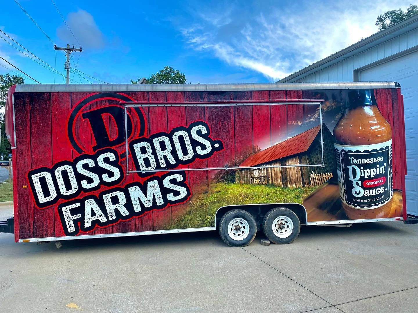 A trailer with branding for Doss Bros. Farms featuring a red wooden background, a barn, a Tennessee Dippin' Original Sauce bottle, and farm imagery.