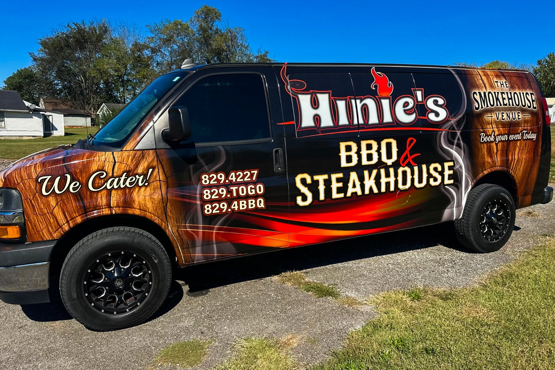Delivery van advertising Aime's BBQ and Steakhouse, with a wood grain background and text for contact numbers, featuring a red flame and smoke design.