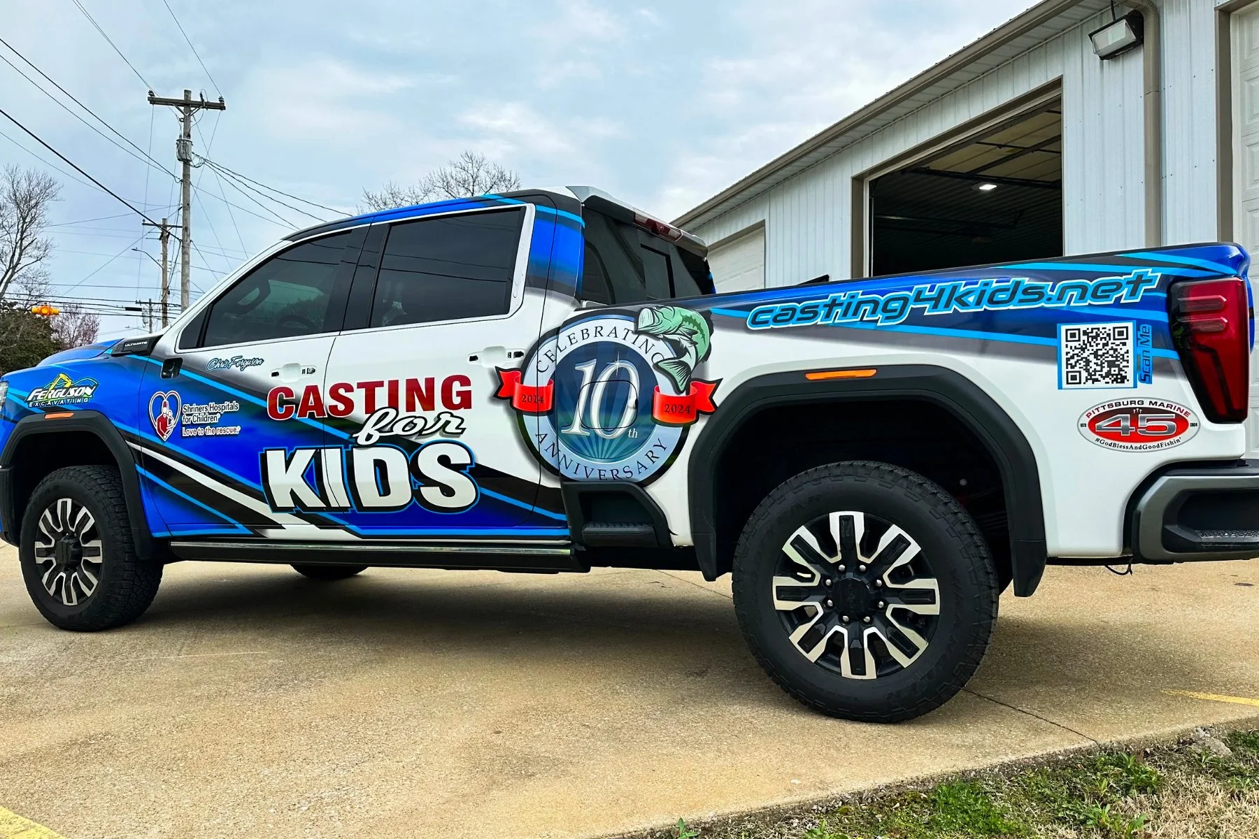 A pickup truck decorated with colorful graphics and text promoting a kids' casting event, celebrating its 10th anniversary from 2014 to 2024, parked outside a building.