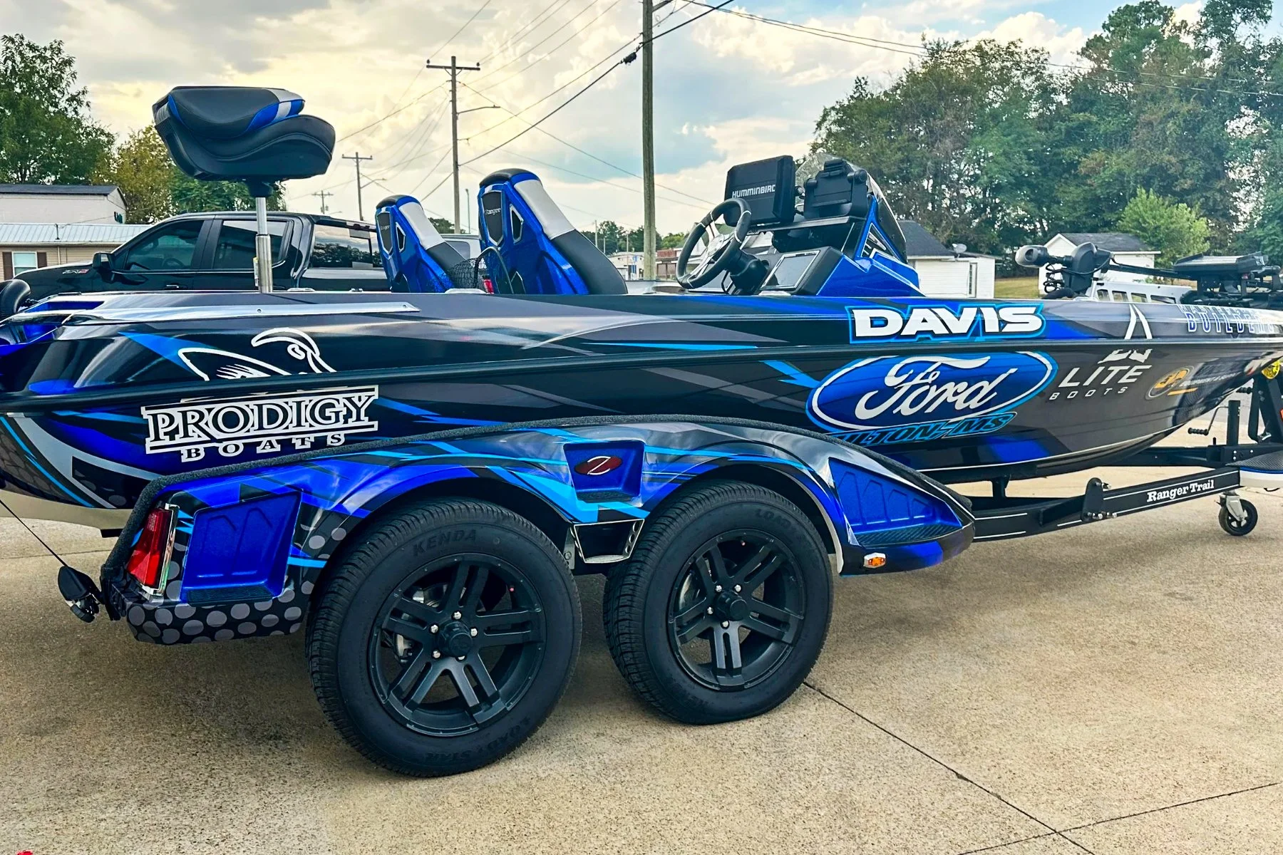 Blue and black racing boat on a trailer, with sponsorship decals, parked outdoors on a paved surface.