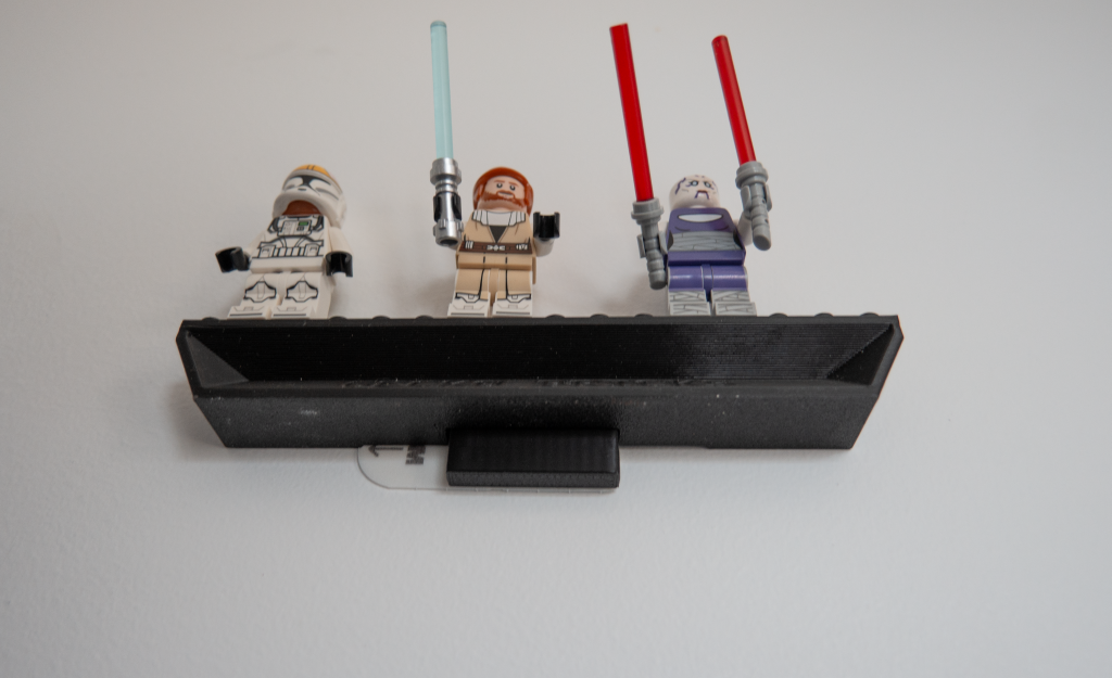 Three LEGO Star Wars minifigures with lightsabers standing on a black holder against a white background.