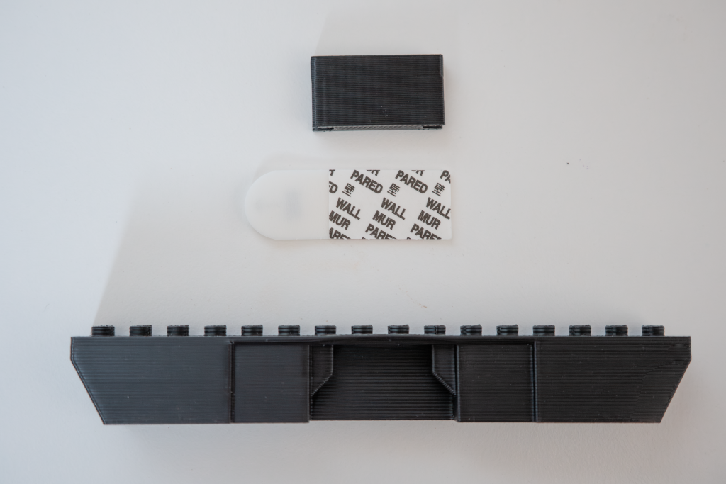 Disassembled LEGO brick with various parts, including a large black piece, a smaller black piece, a white sticker sheet, and a small white oval-shaped piece, all on a white background.