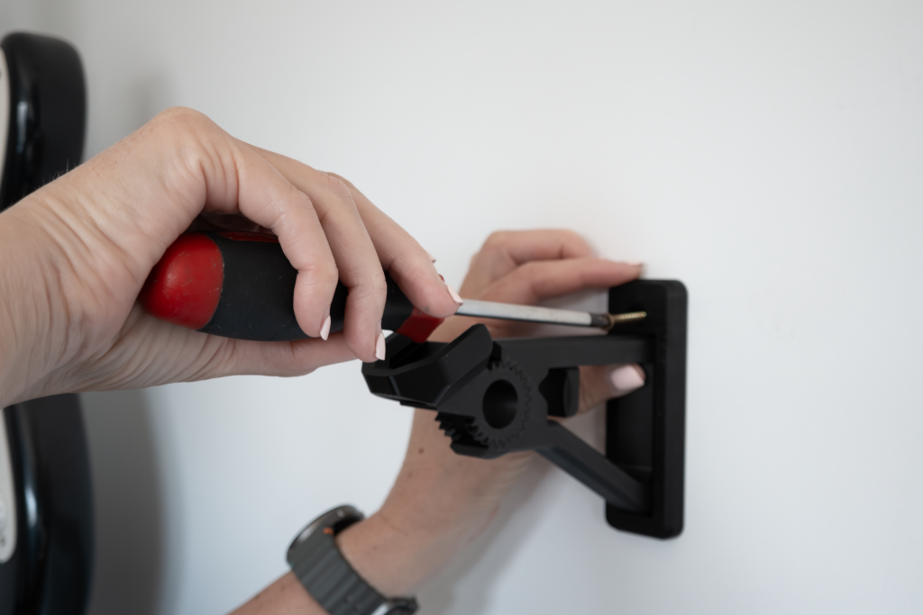 Person using a screwdriver to mount a black bracket on a white wall.