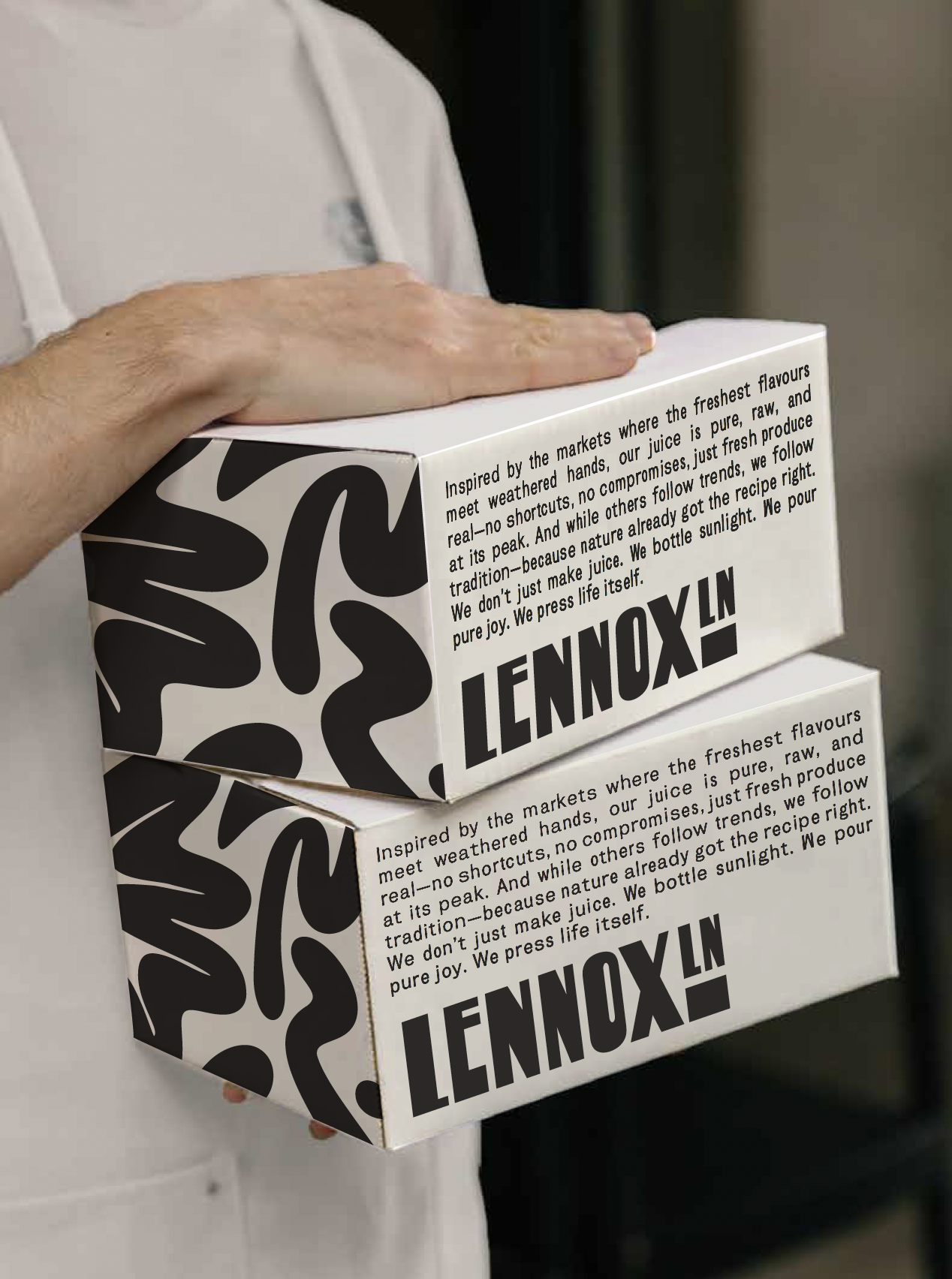 Two boxes of LlynoX juice, with a person's hand holding them. The boxes have black and white abstract designs and text about the product's inspiration and qualities.