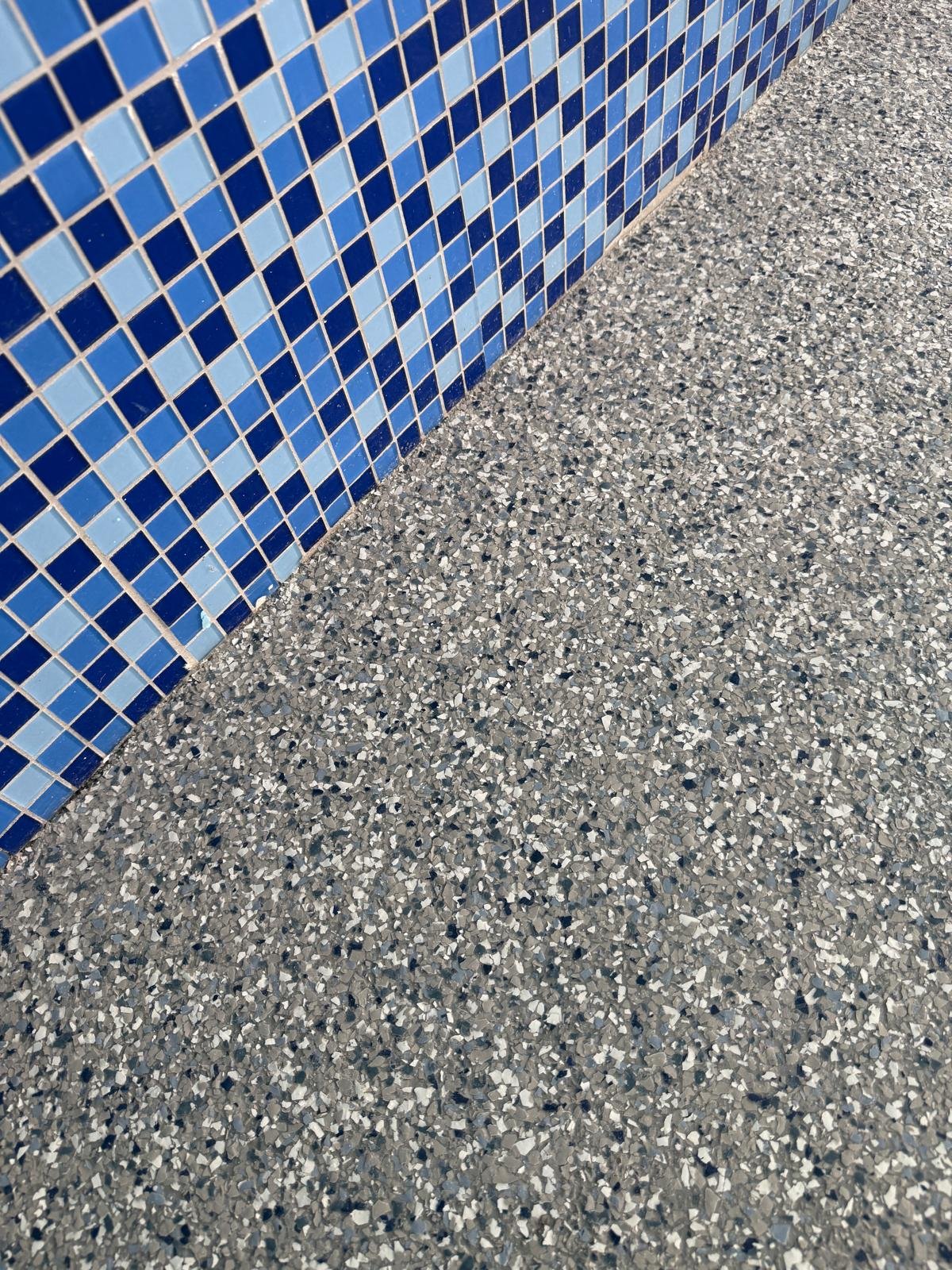 Close-up of a blue mosaic tile wall and a speckled gray terrazzo floor.