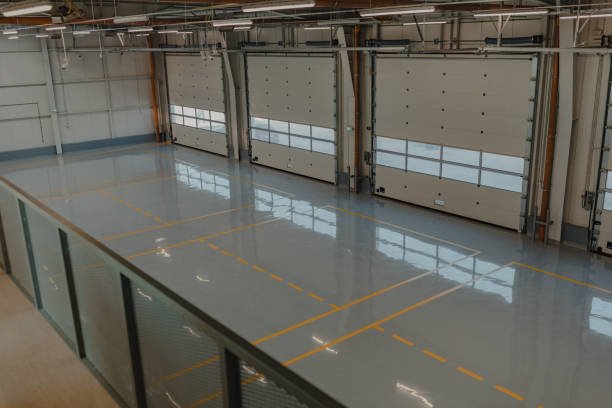 Interior of an empty industrial warehouse with high ceilings and three large closed garage doors.