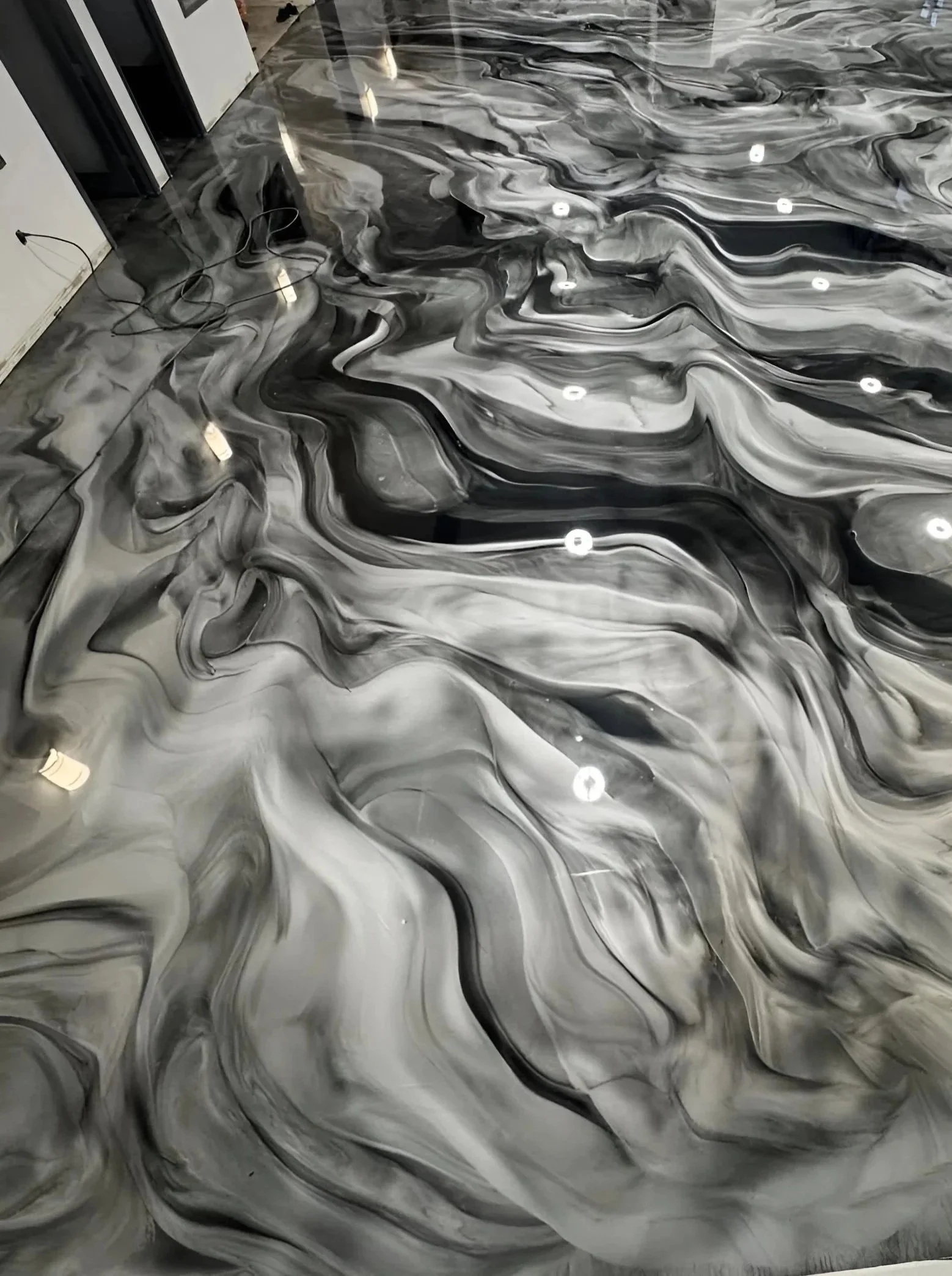 Marble floor with black, white, and gray swirls and reflections of ceiling lights.
