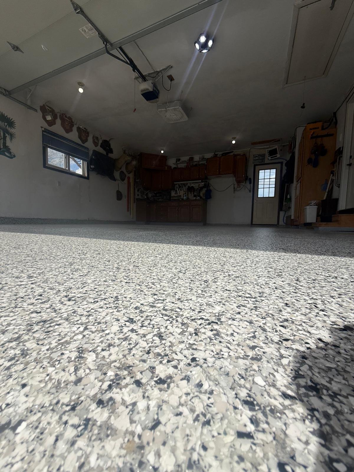Interior of a garage with a speckled epoxy floor, cabinets, and a window on the left wall.