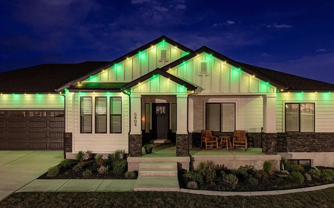 A modern house decorated with green Christmas lights outside at night.