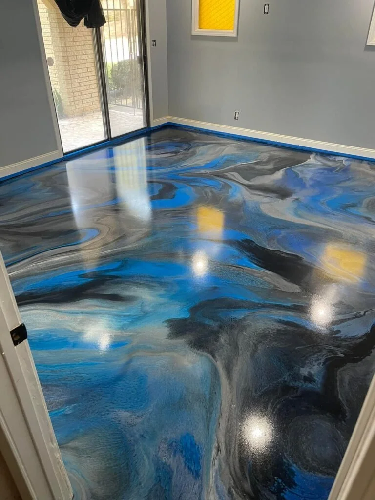 Room with a swirl-patterned epoxy floor featuring black, blue, and white colors, next to a sliding glass door and decorated with yellow and white framed windows.