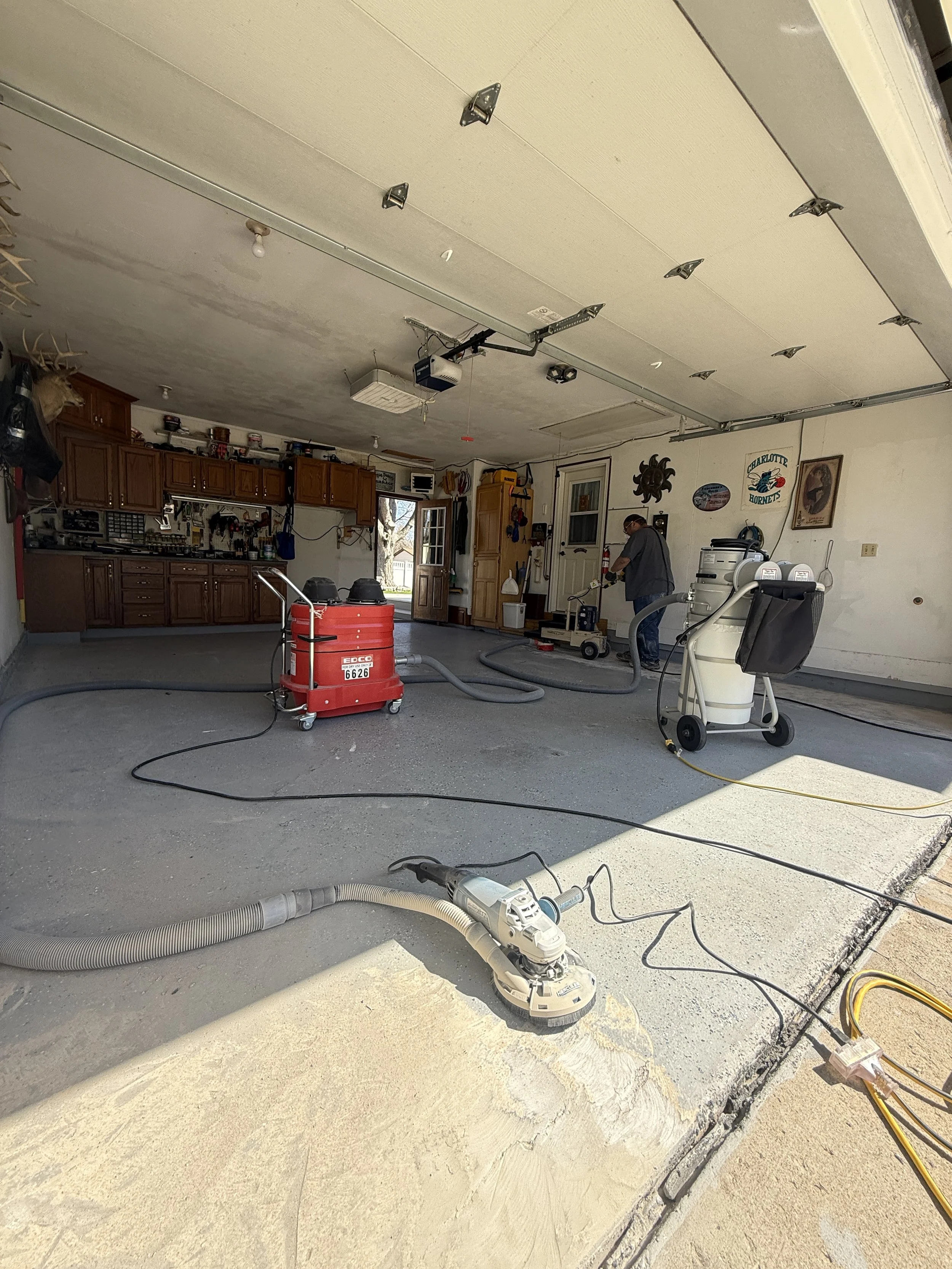 Person working on a garage door repair with tools and equipment around, garage with cabinet storage and vehicles outside.