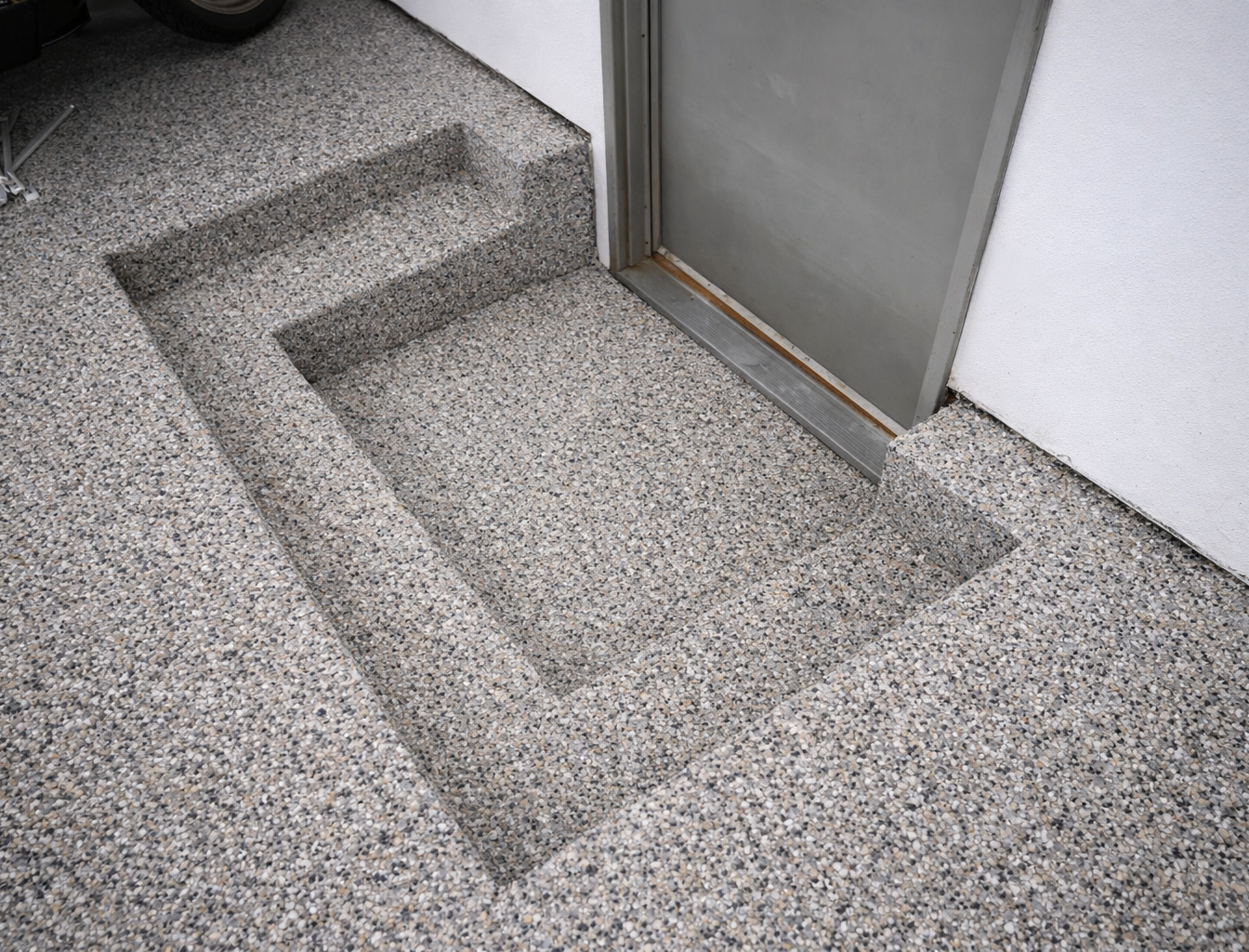Concrete steps with embedded doormat area next to a metal door in a white wall.