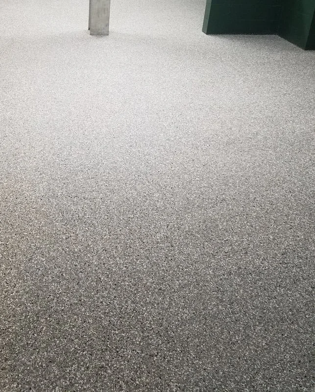 Image of a textured grey carpeted floor with a metal pole and a green waste bin.