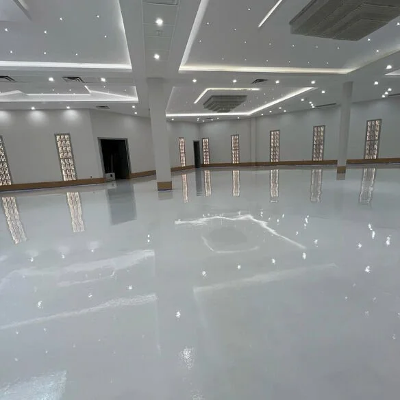 Empty spacious room with glossy floor, white walls, multiple windows, and ceiling lights.