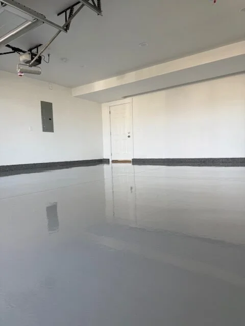 Empty garage with white walls, gray baseboards, a closed white door, and a reflective polished concrete floor.