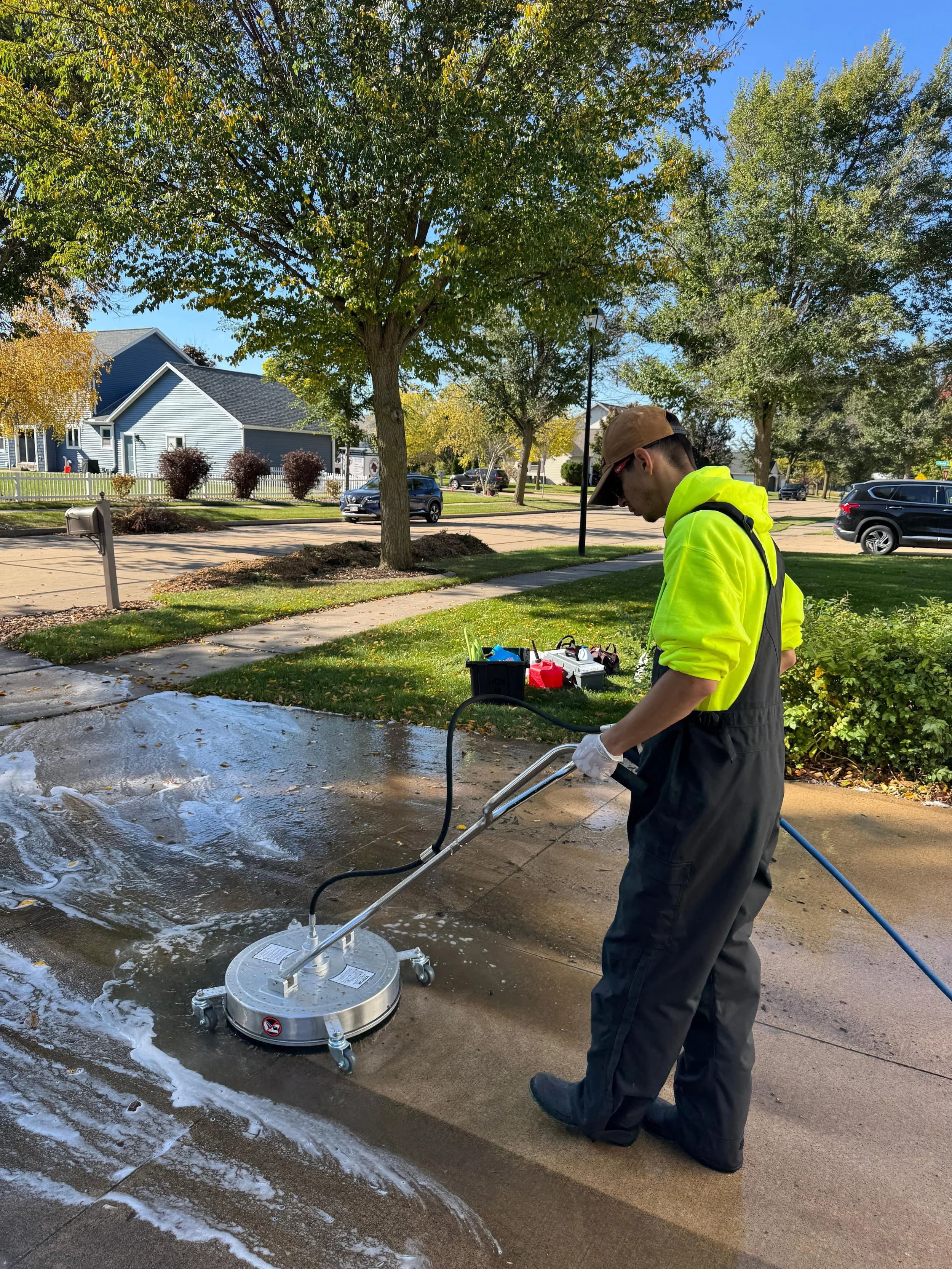Person pressure washing a concrete driveway on a sunny day.