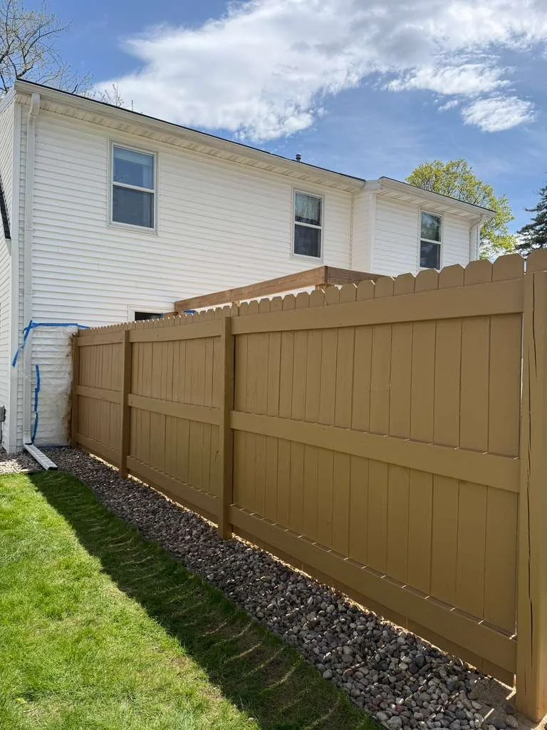 New wooden privacy fence installed in a backyard with a white house and a blue sky background.