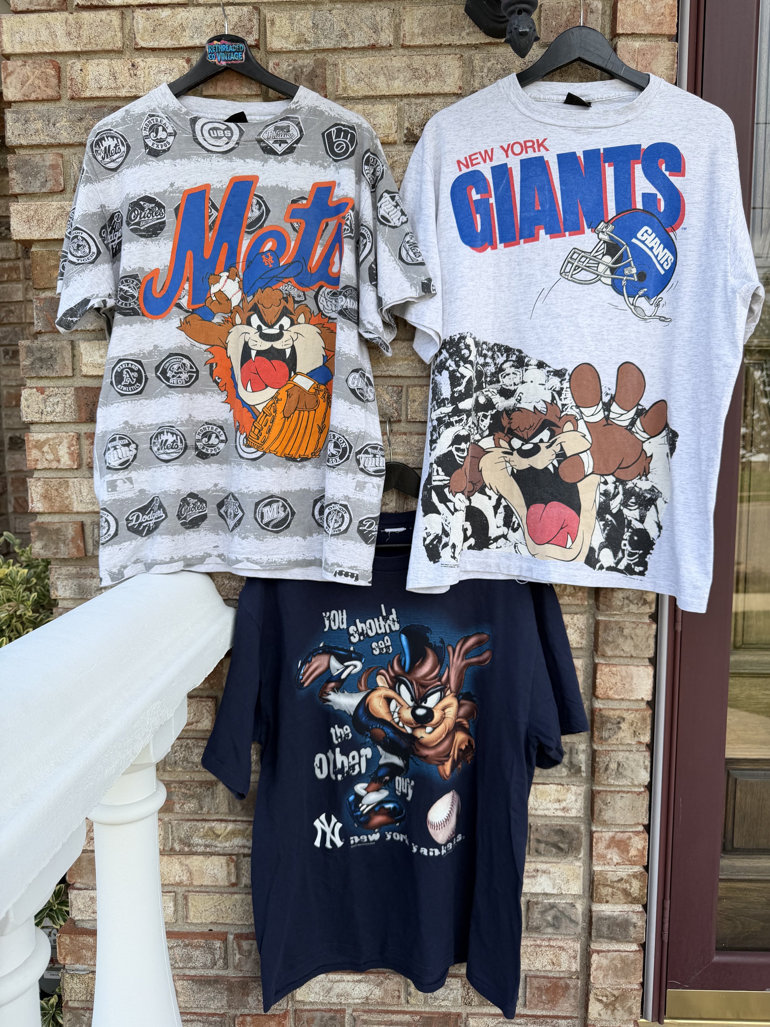 Vintage New York Mets, Yankees and New York Giants graphic T-shirts featuring Looney Tunes characters displayed on a brick wall.