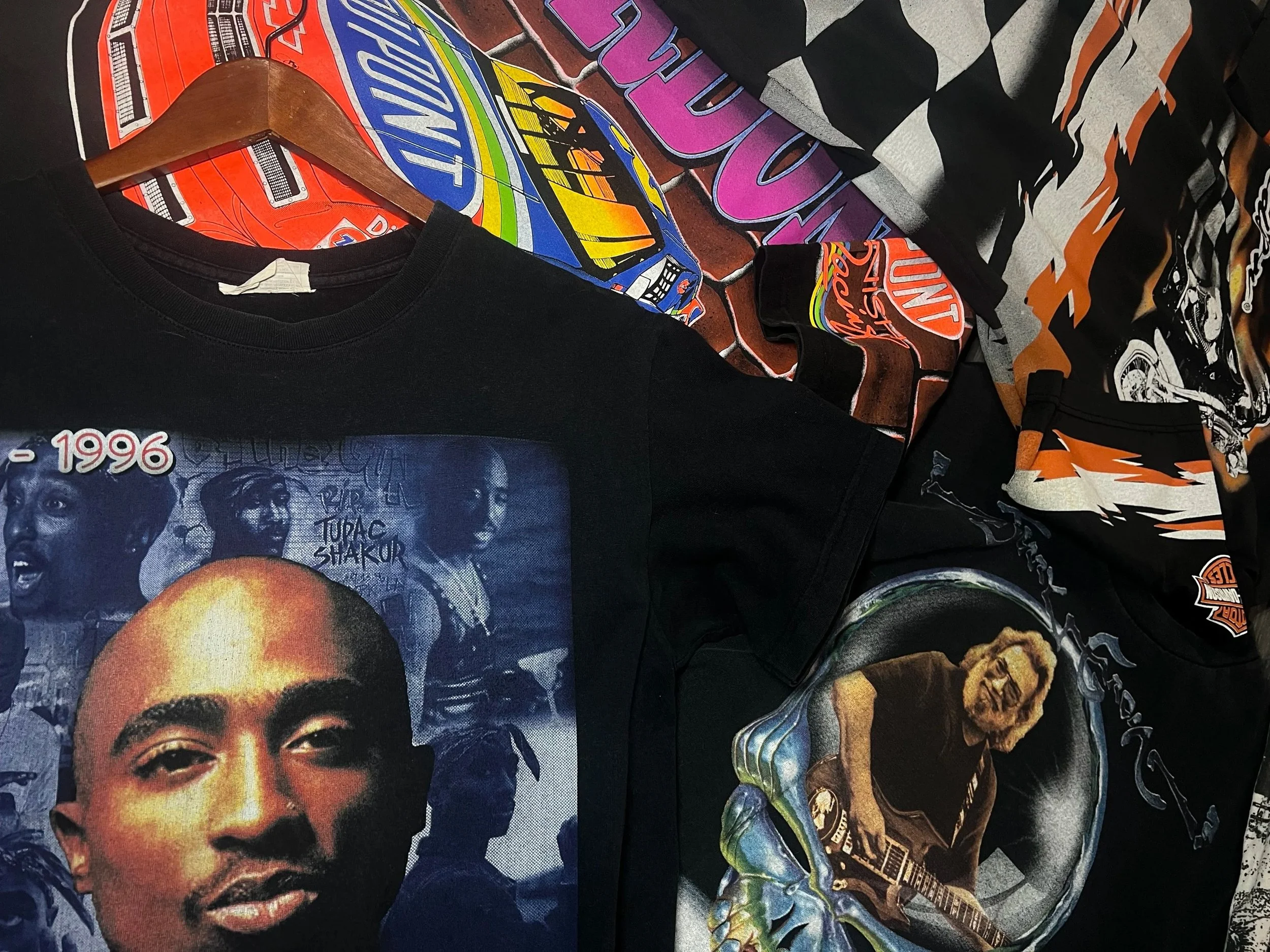 Collection of vintage band and music t-shirts featuring images of Tupac Shakur, Jimi Hendrix, and others, along with patches and graphic designs.
