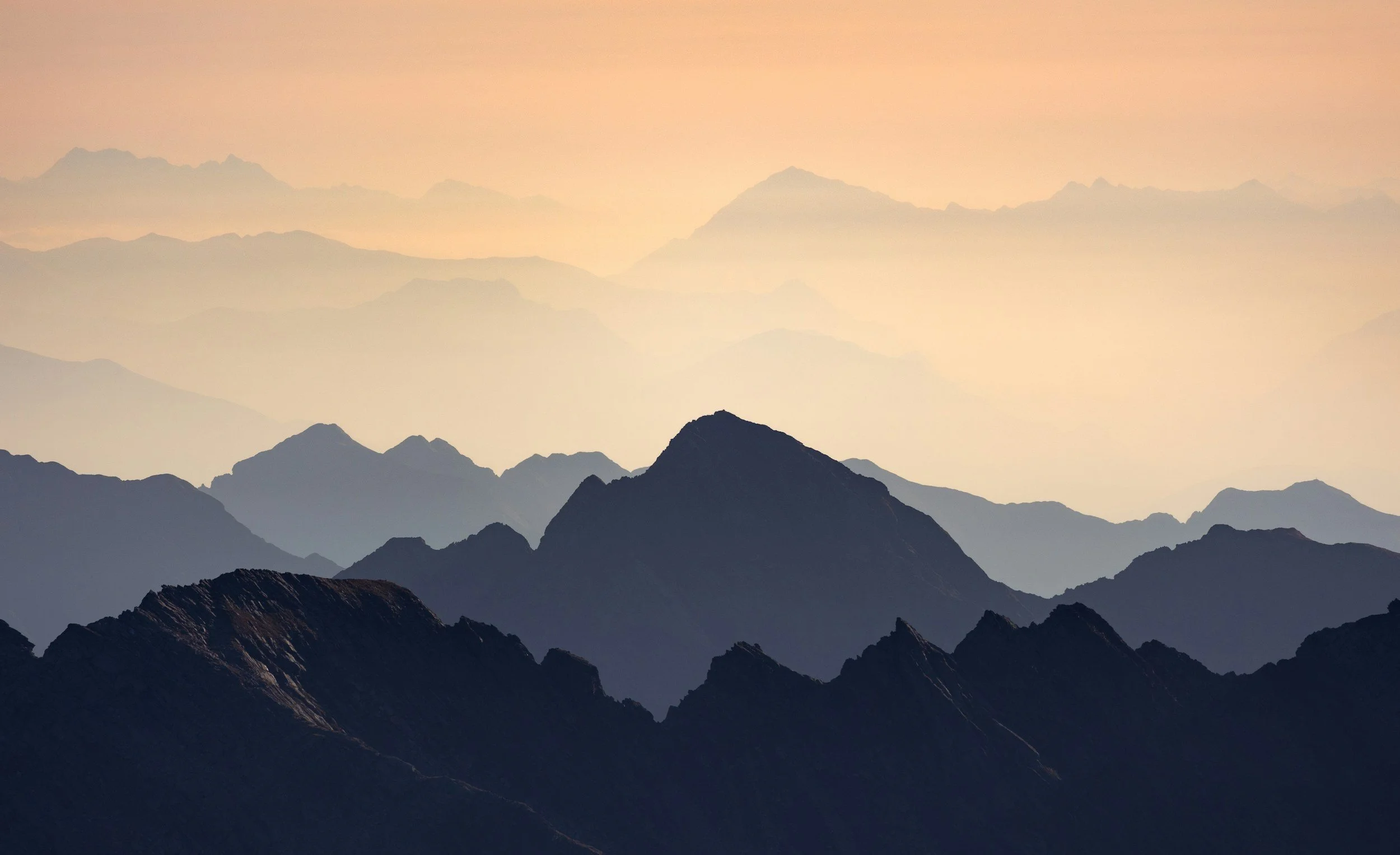 Silhouette of mountain peaks against a pastel sky with multiple haze layers creating a sense of depth.