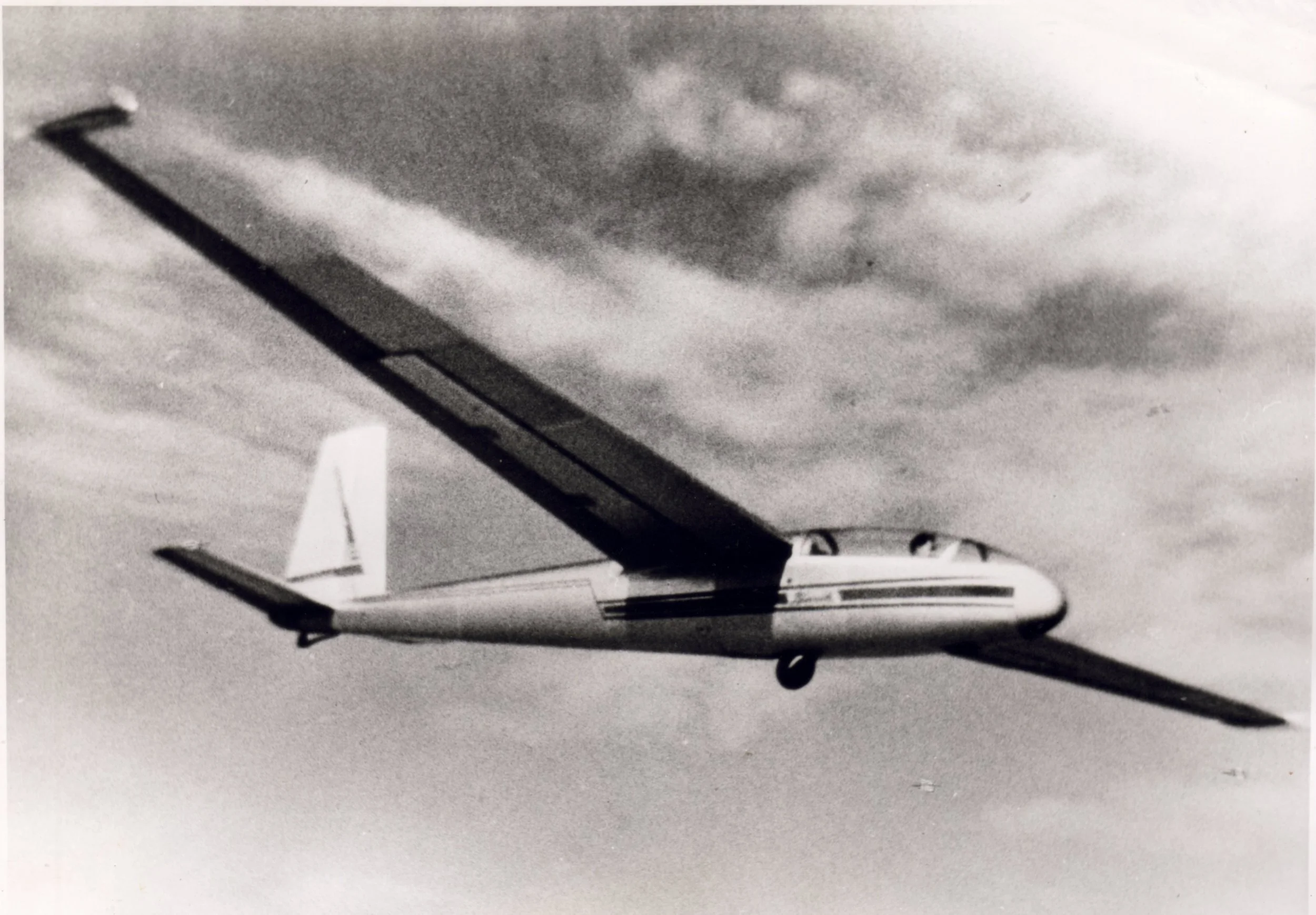 Black and white photo of a vintage airplane flying in the sky with clouds.