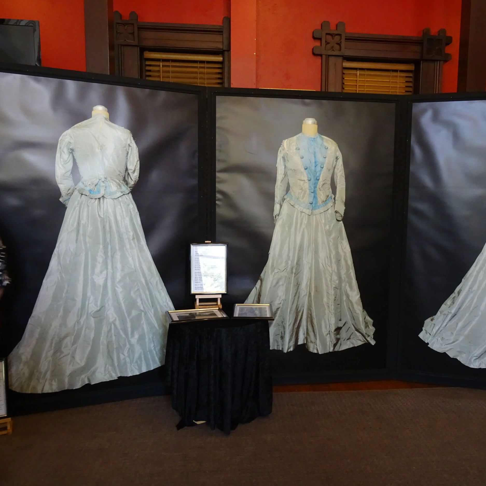 Display of historical dresses on mannequins behind black panels at an exhibit.
