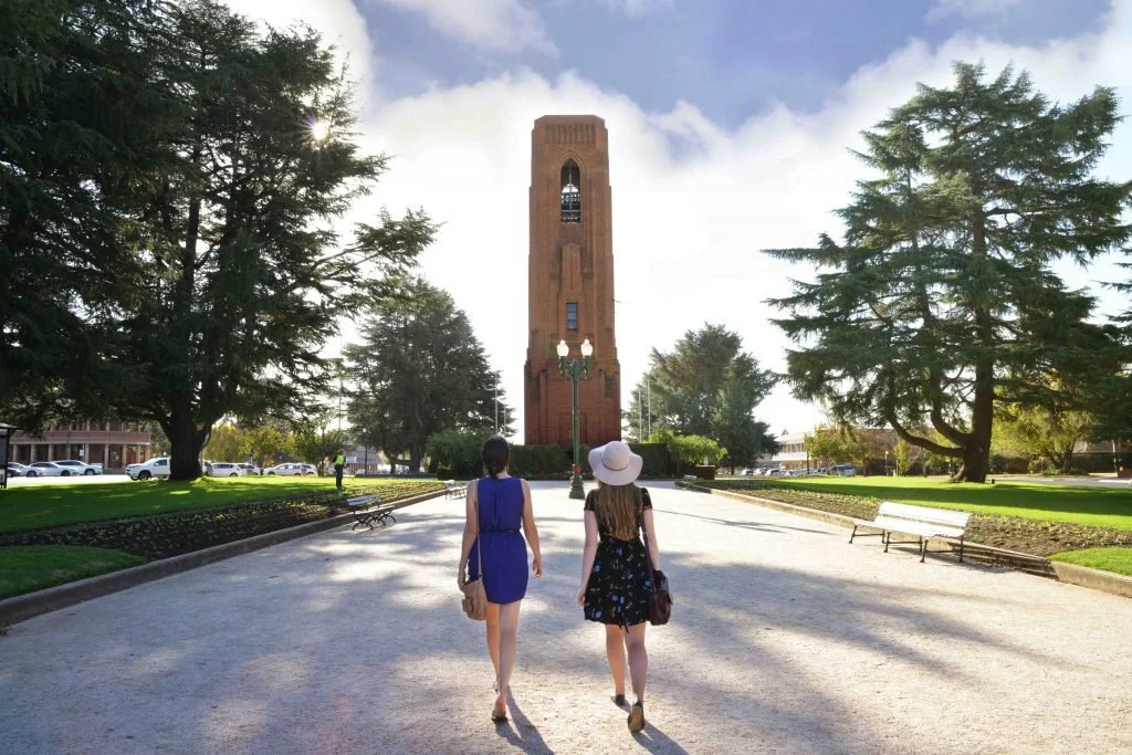 Two women are walking in the centre of Kings Parade towards the Carillon