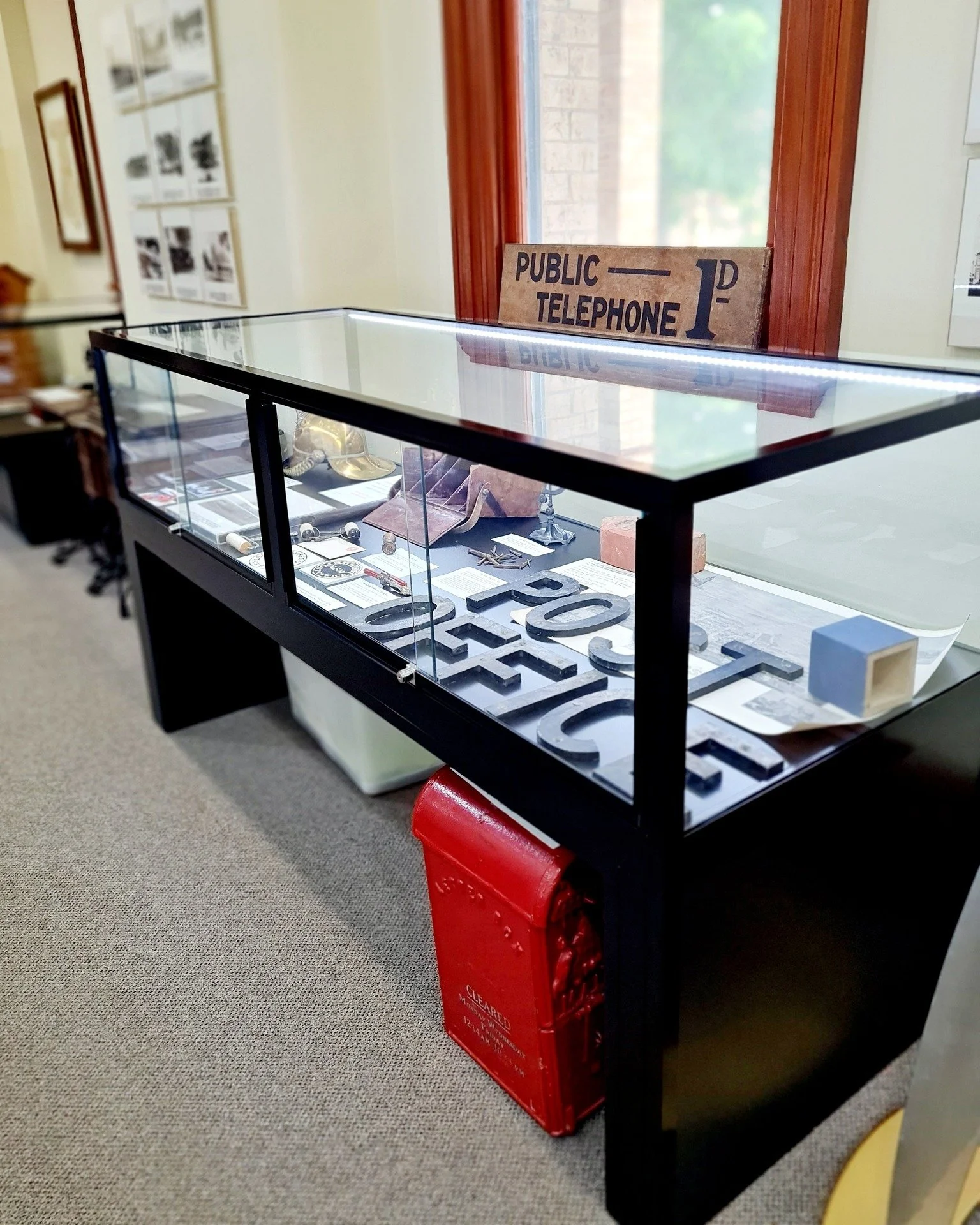 Display case with historical artifacts and signs, including a vintage public telephone sign, in a museum setting.