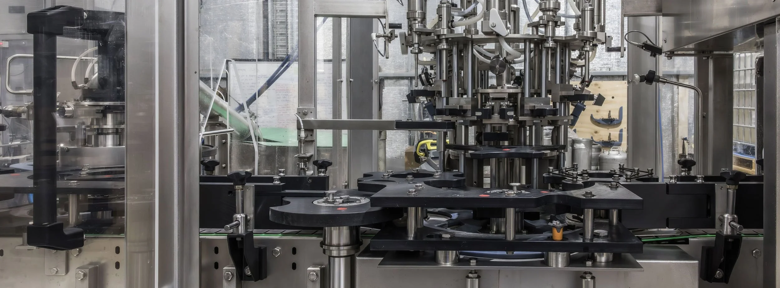 A sophisticated stainless steel laboratory or industrial machine with various mechanical parts, knobs, and clamps, enclosed in a transparent protective casing.