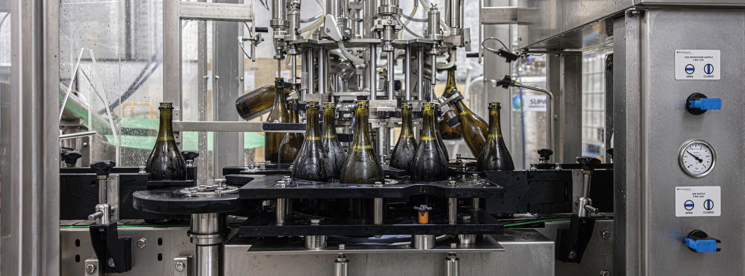Automated bottling machine filling glass sparkling bottles in the Kilchurn factory environment.