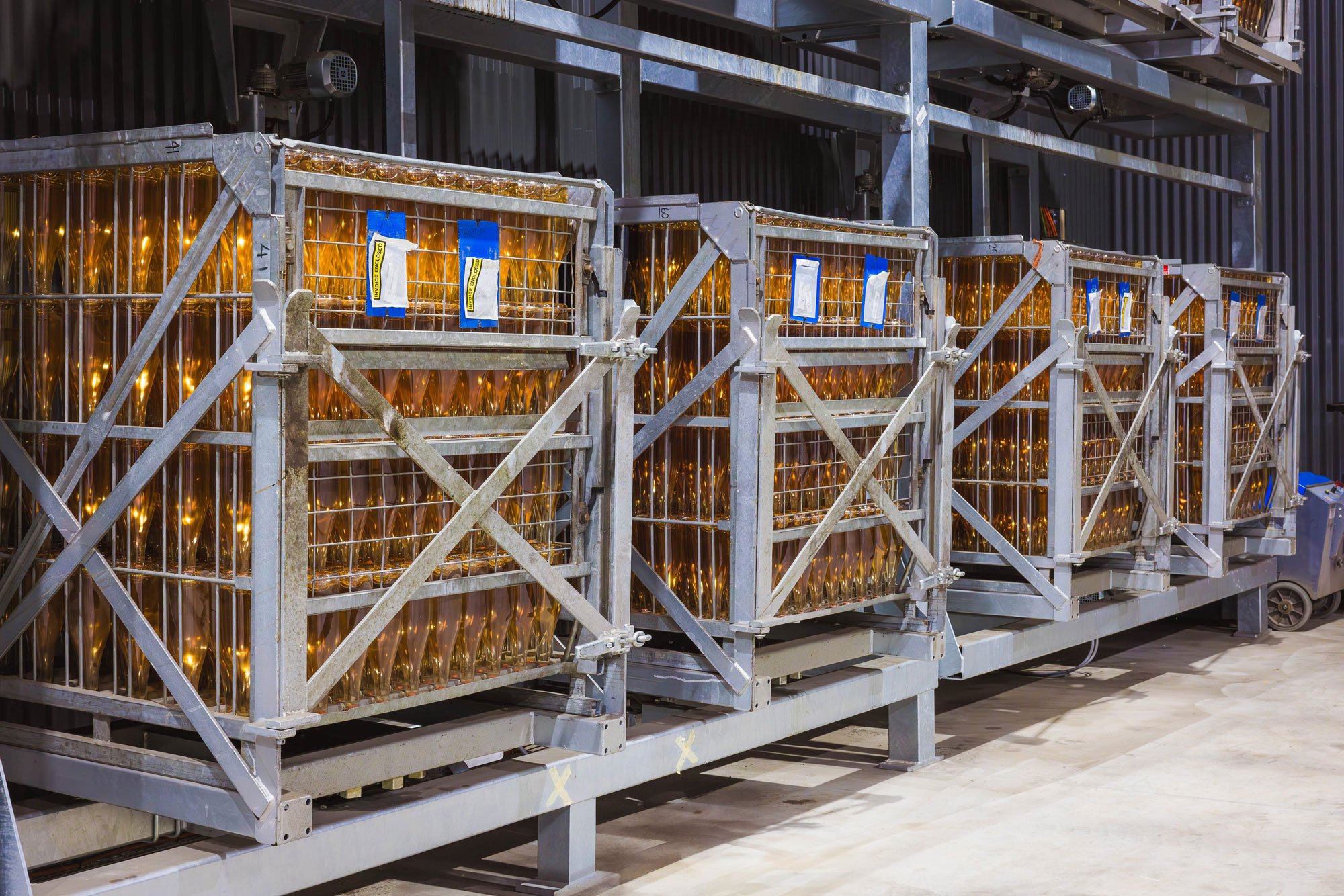 Metal storage cages filled with wrapped sparkling wine bottles in an industrial setting.