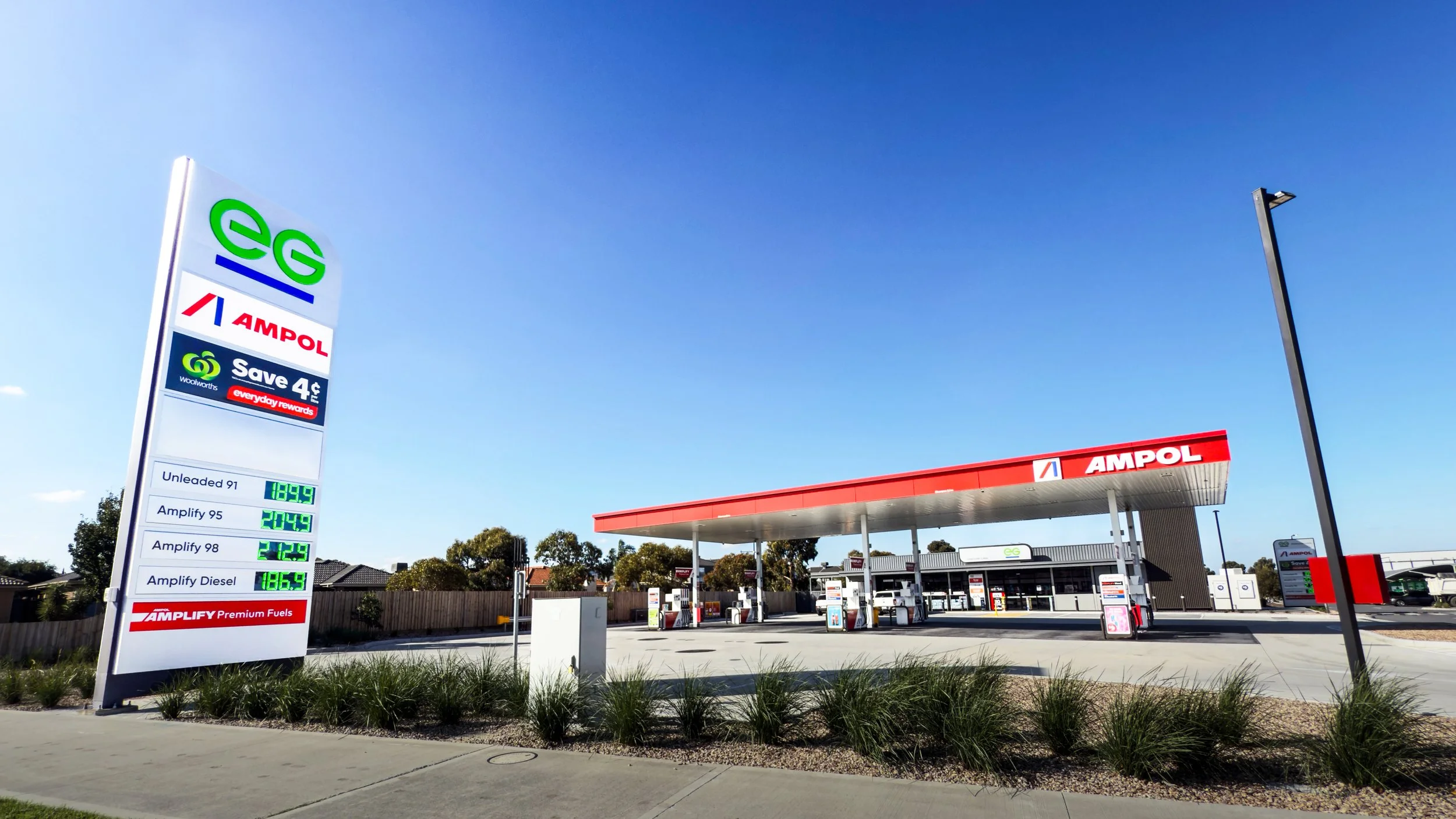 A gas station with a large illuminated sign showing fuel prices and a canopy over fuel pumps, with a clear blue sky overhead.