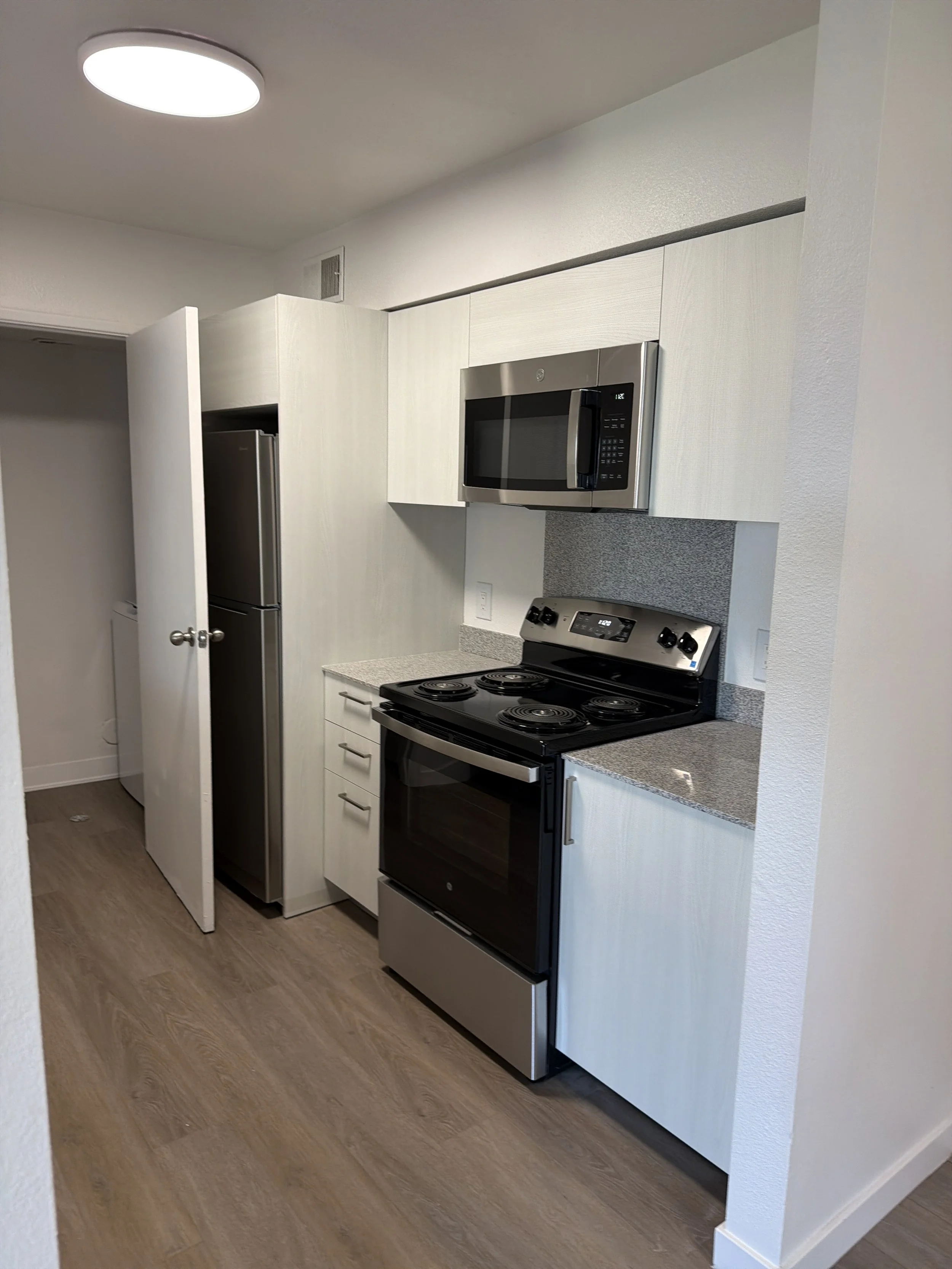 Kitchen with stainless steel appliances including a microwave, stove, and refrigerator, with light-colored cabinets and wooden flooring.