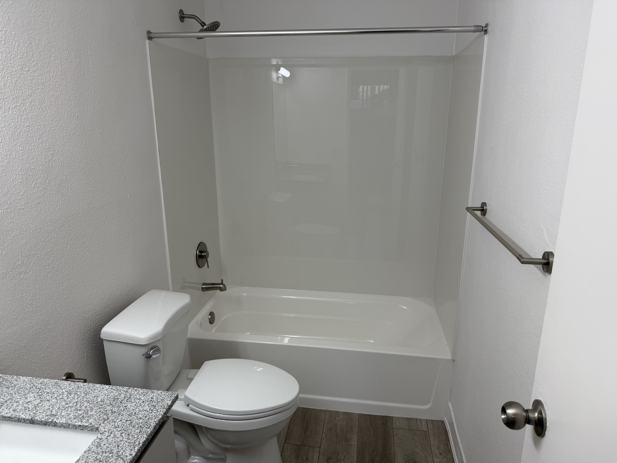 Bathroom with a toilet, a bathtub with a showerhead, a granite countertop, and towel bars on the wall.