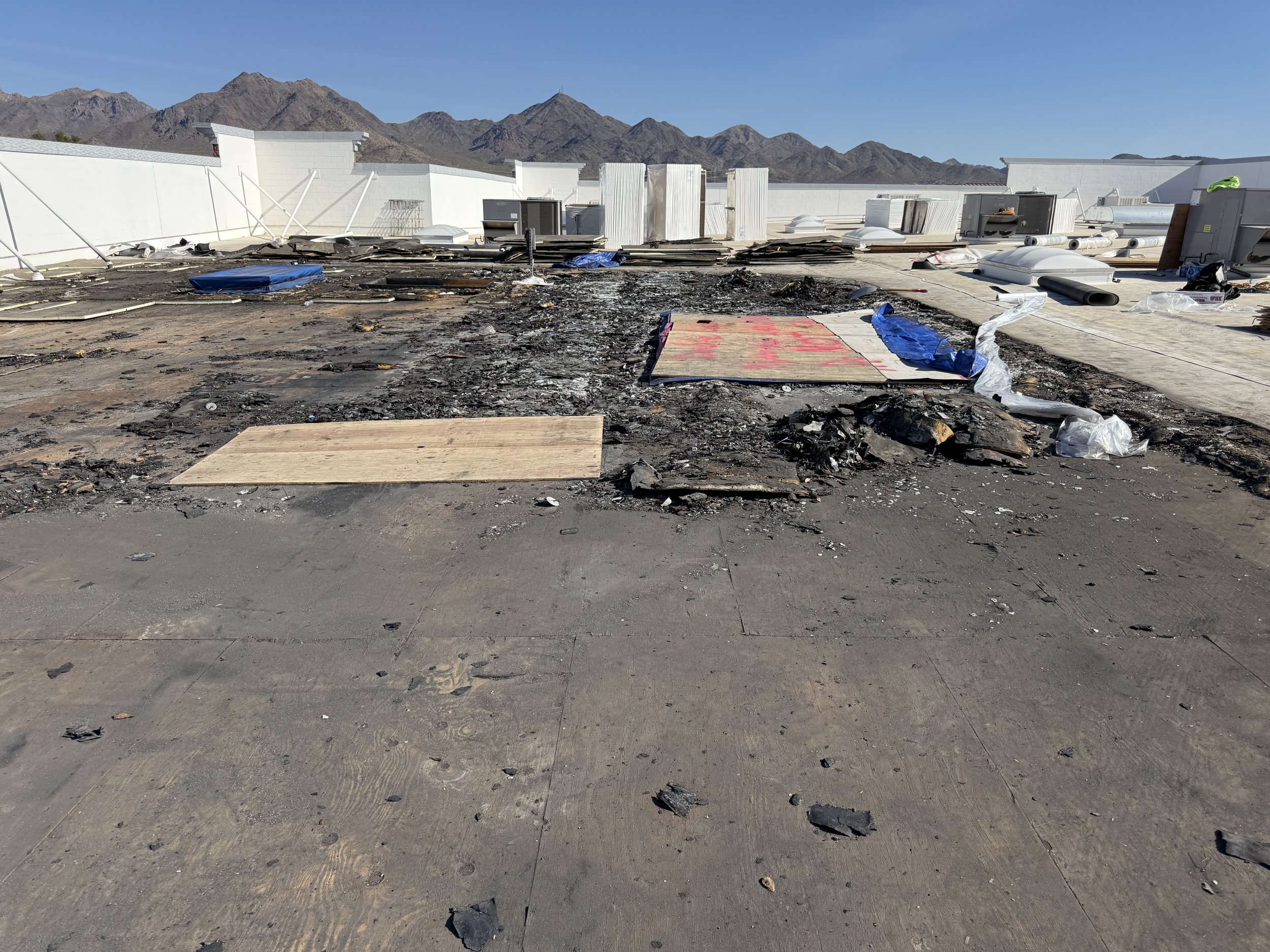 Charred rooftop with burnt debris, damaged materials, and mountains in the background. Commercial Roofing, Insurance