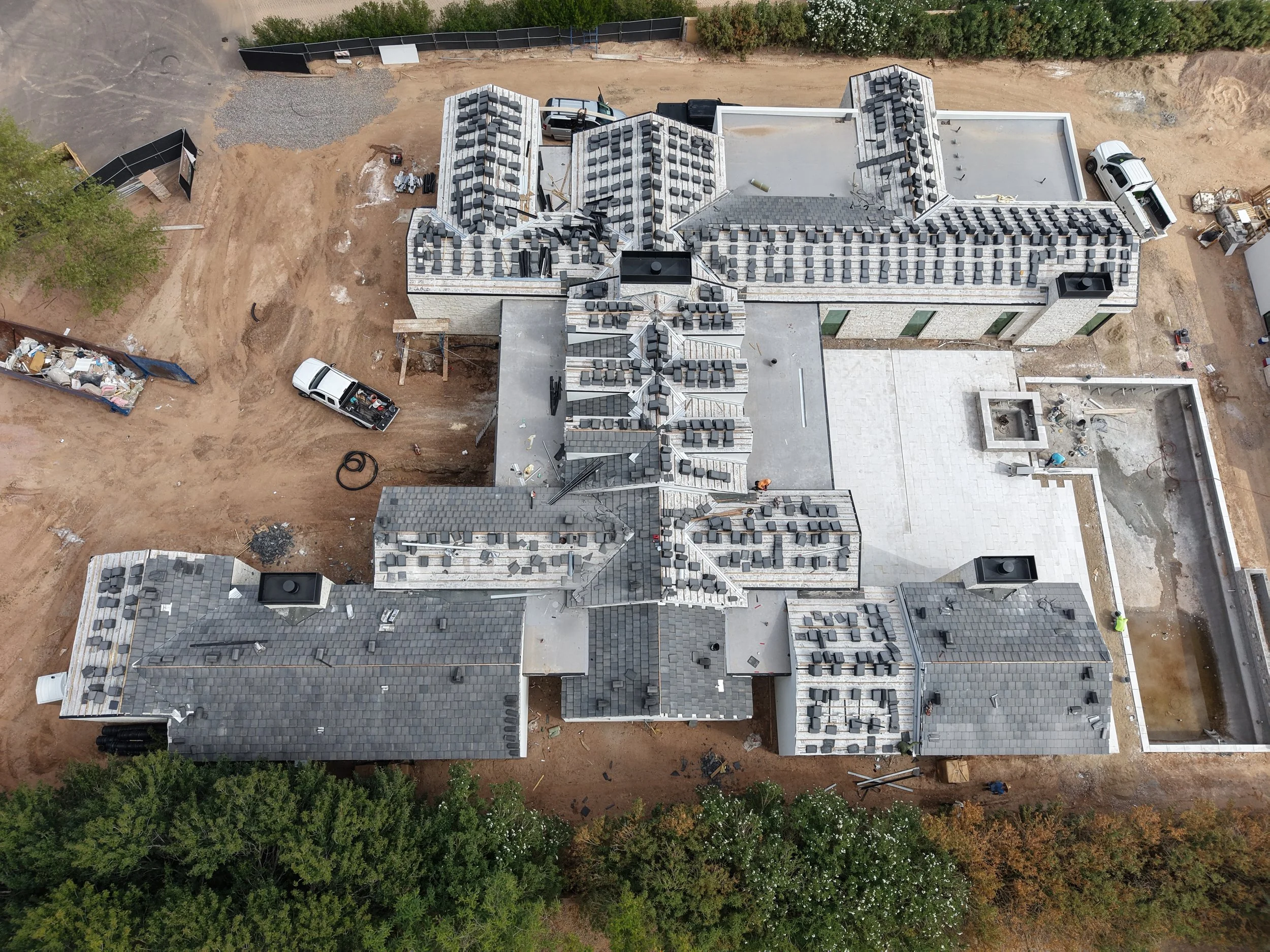 Aerial view of a large house under construction with multiple roof sections, construction materials, trucks, and equipment around the site. Tile Roof system, TPO roof System