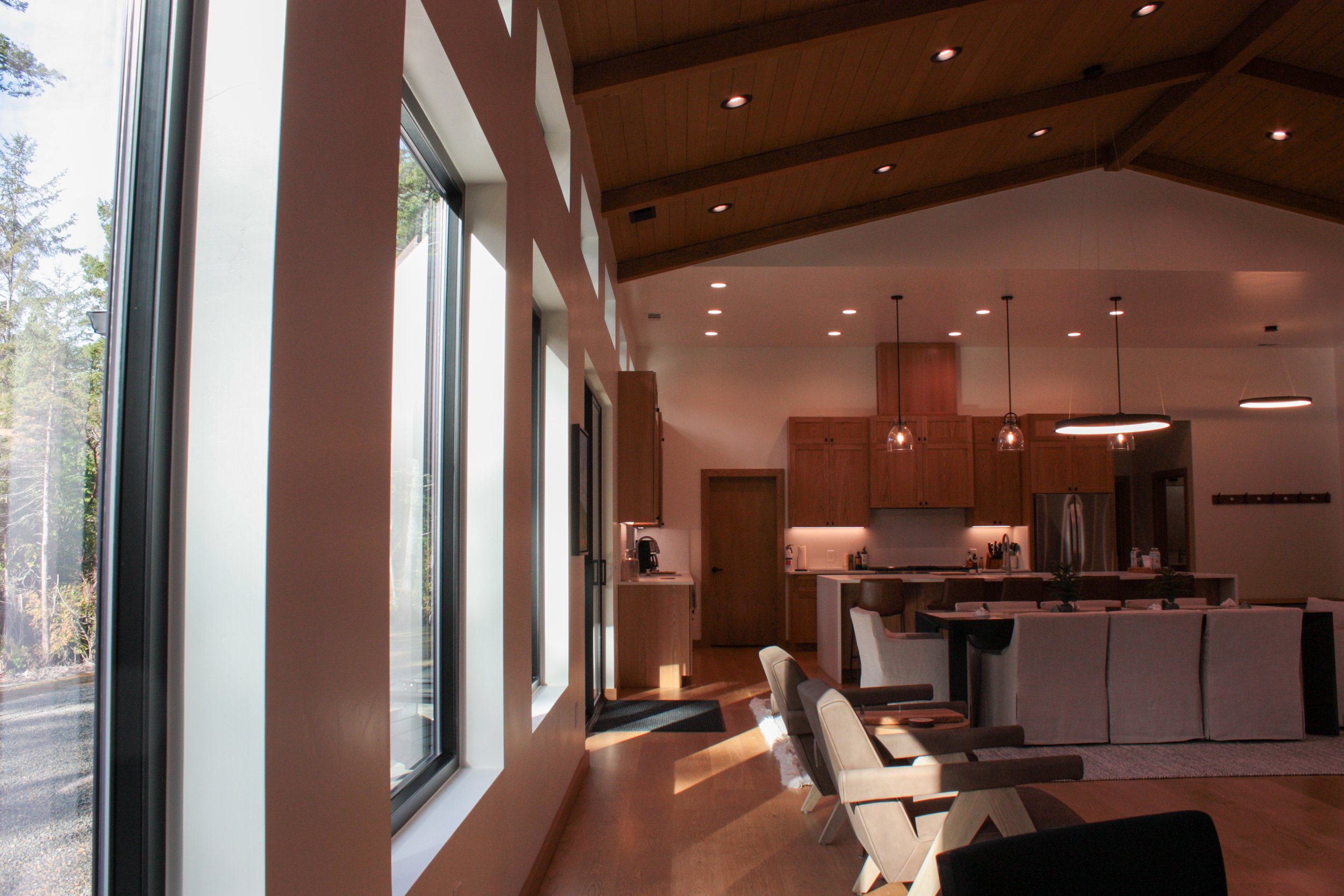 Interior of a modern kitchen and dining area with large windows, wooden ceiling, and contemporary pendant lighting.