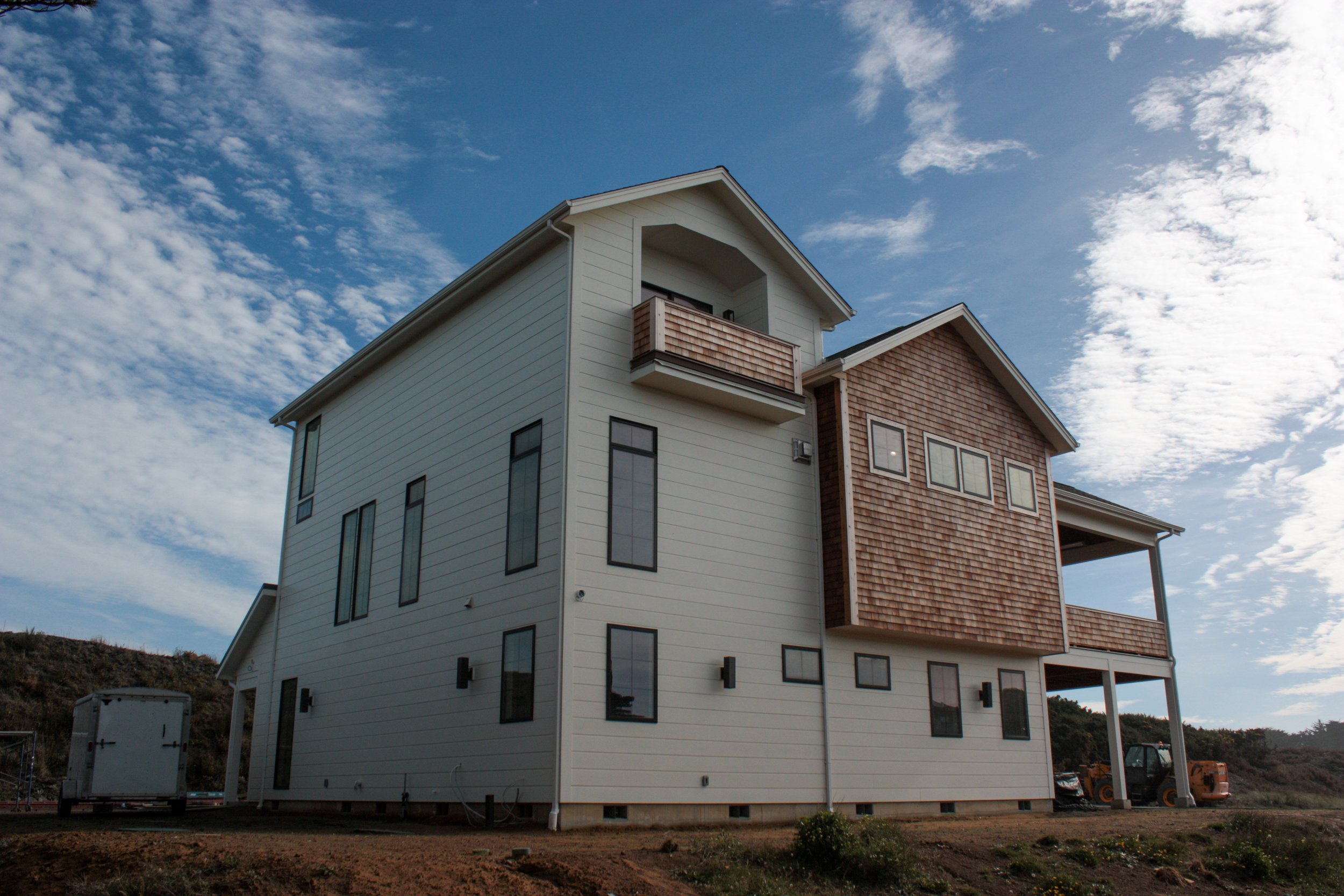 A modern multi-story house with white siding and brown shingle accents, set against a partly cloudy sky.