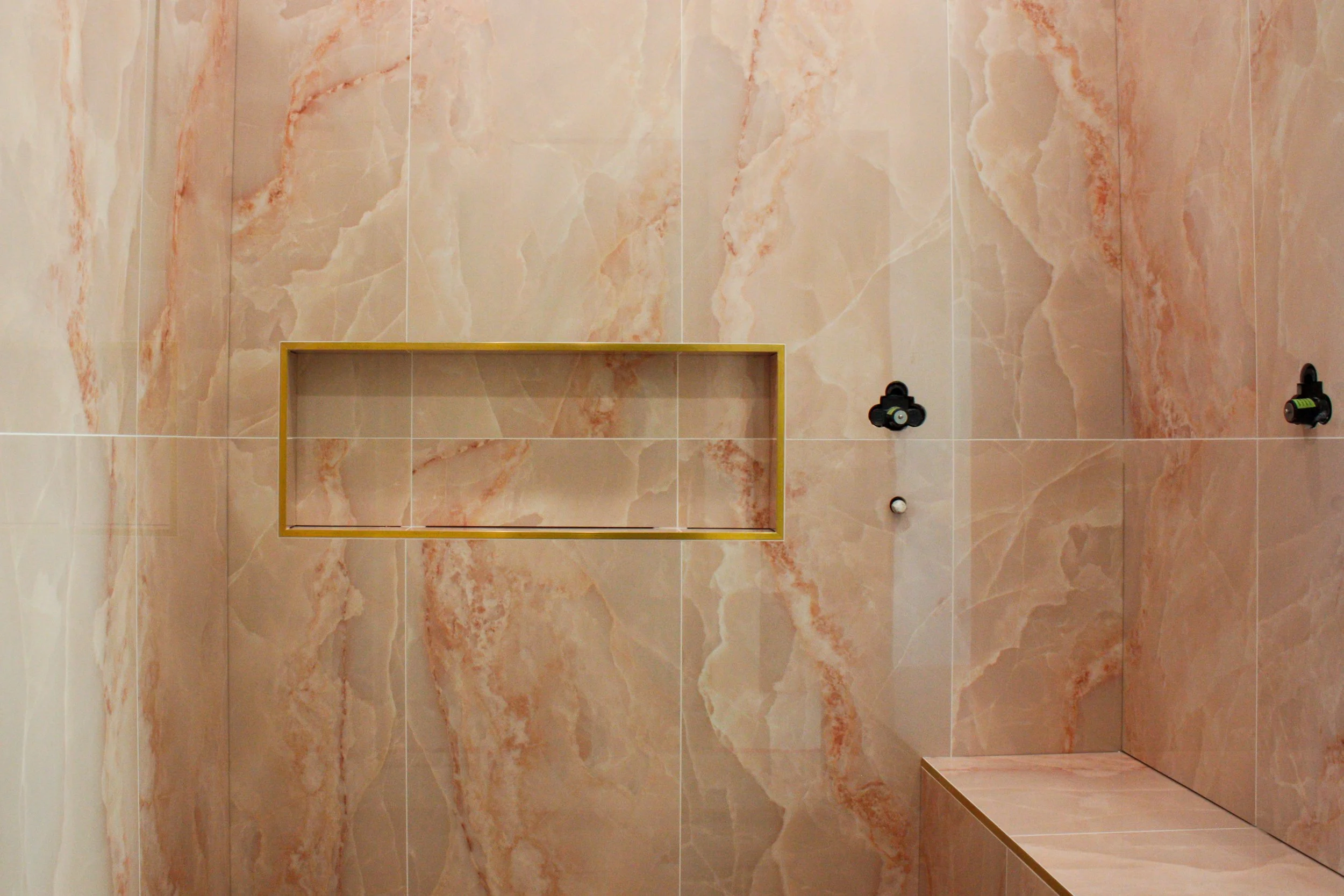 Bathroom shower area with peach-colored marble tiles, a built-in niche with a yellow frame, and black plumbing fixtures.