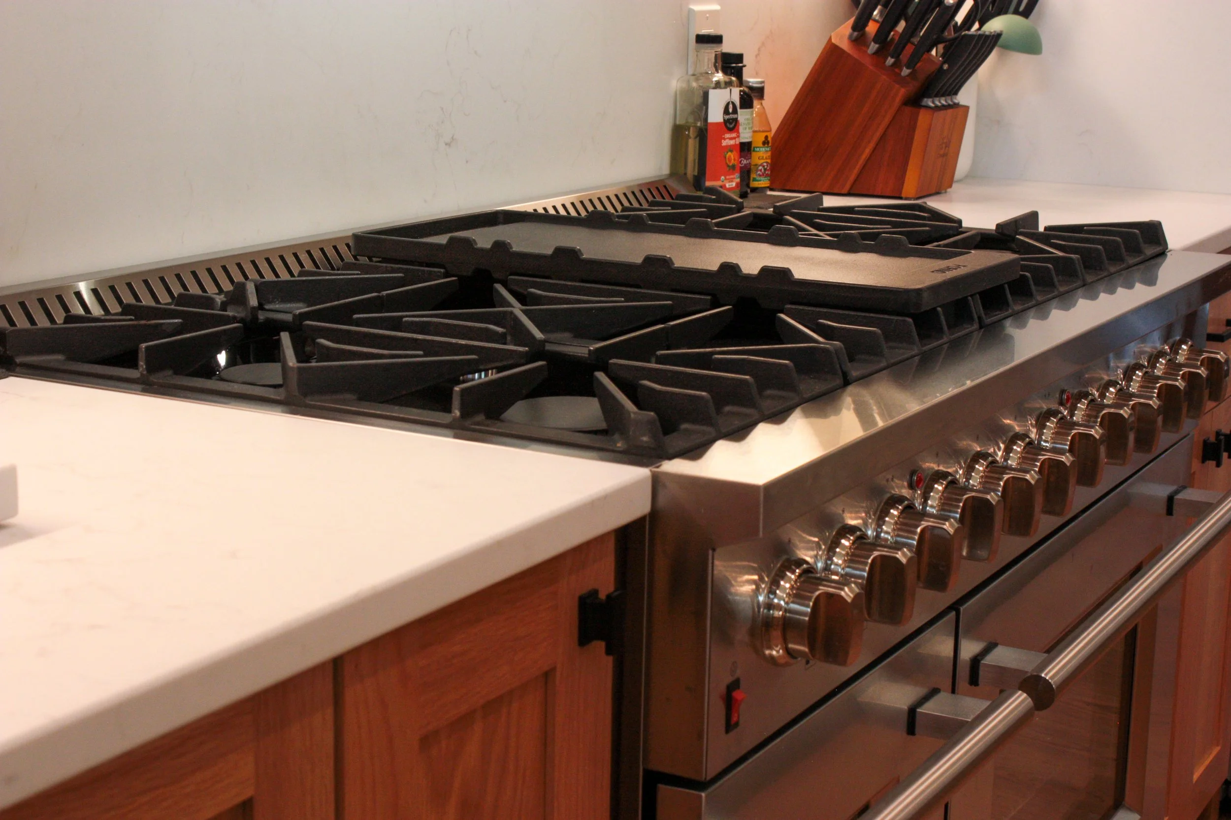A stainless steel gas stove with multiple burners, a wooden knife block, and bottles of cooking oils and sauces on a kitchen countertop.