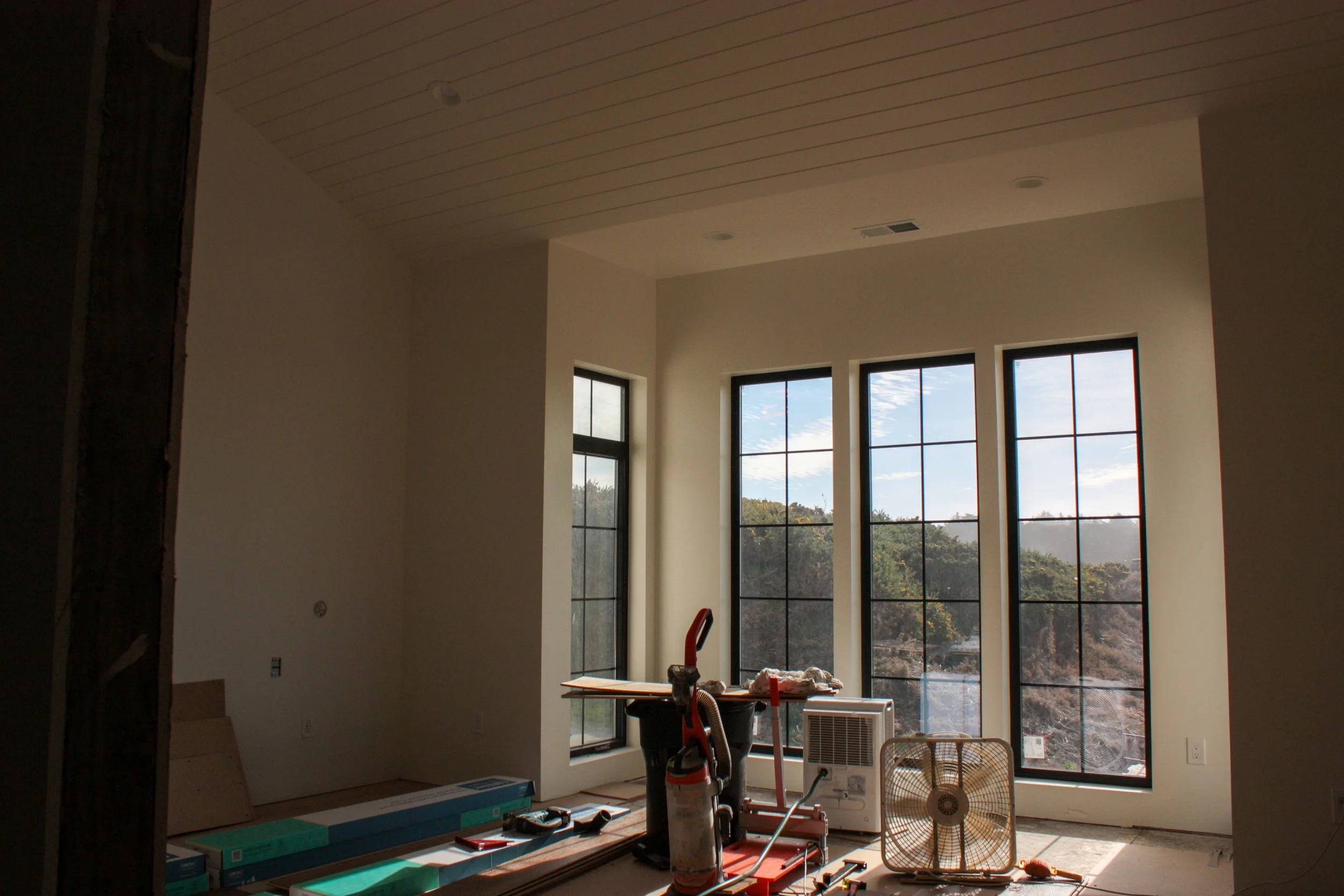 Interior of a room under construction, featuring large windows and construction tools on the floor.