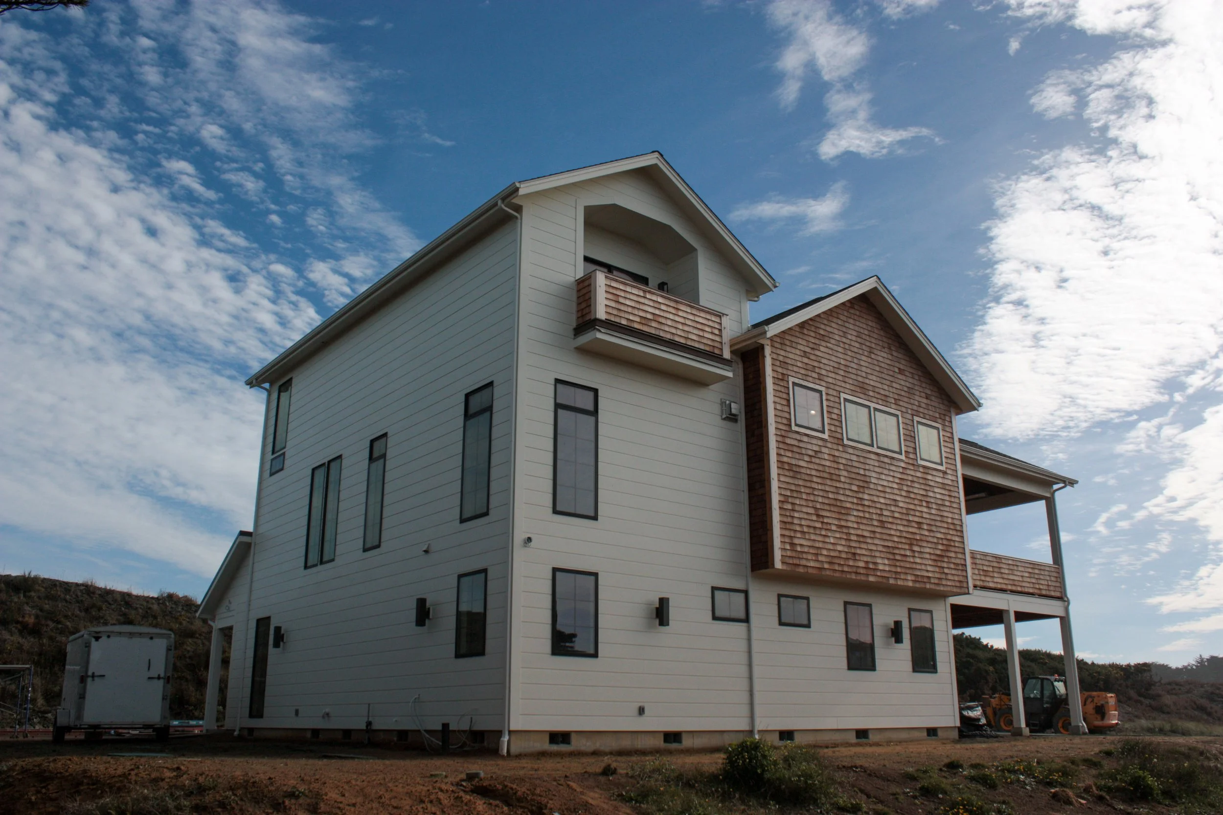 A multi-story modern house with white siding and wooden accents, set against a partly cloudy sky.