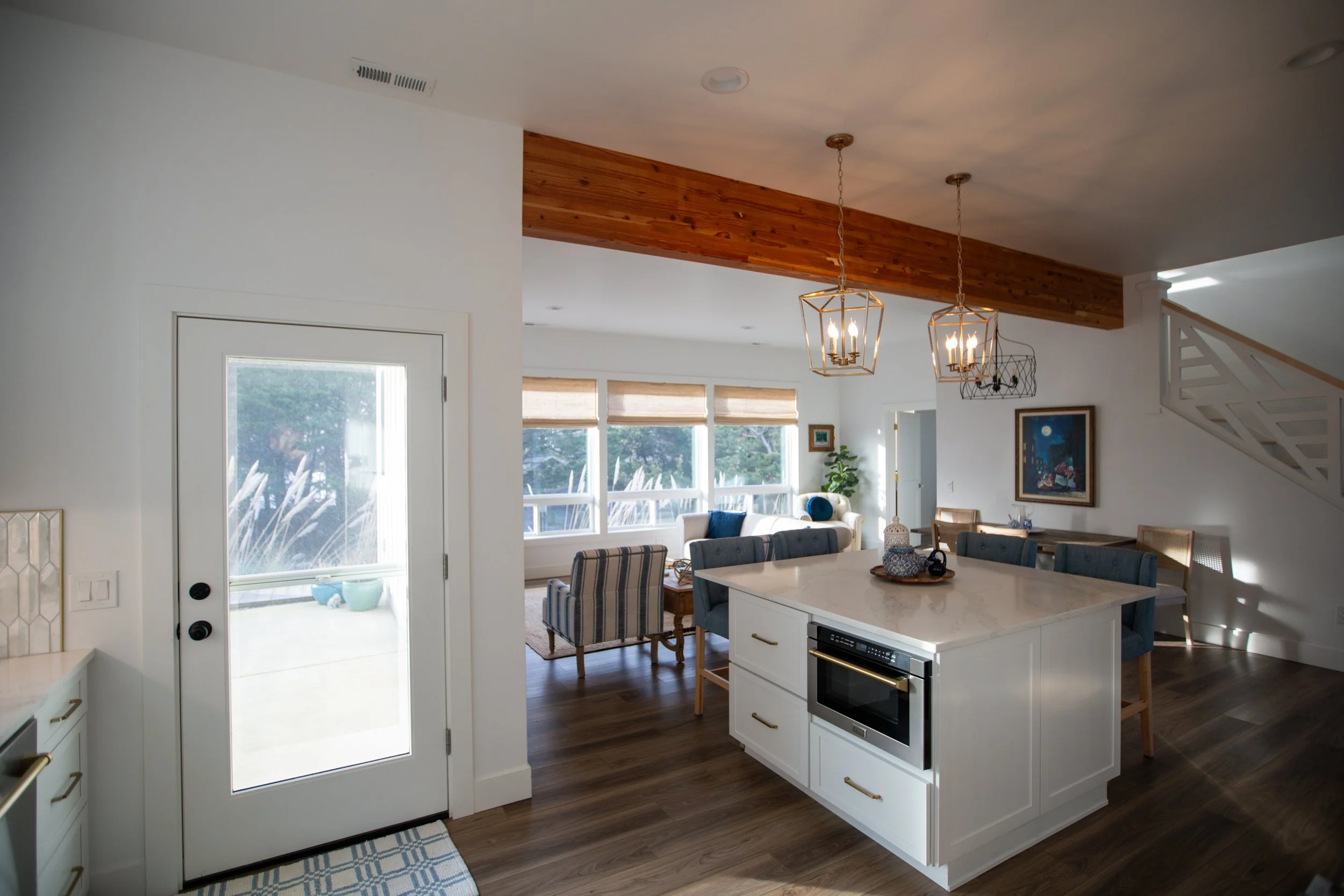 Open-concept living room and kitchen with large windows, white walls, wooden floors, and modern furniture