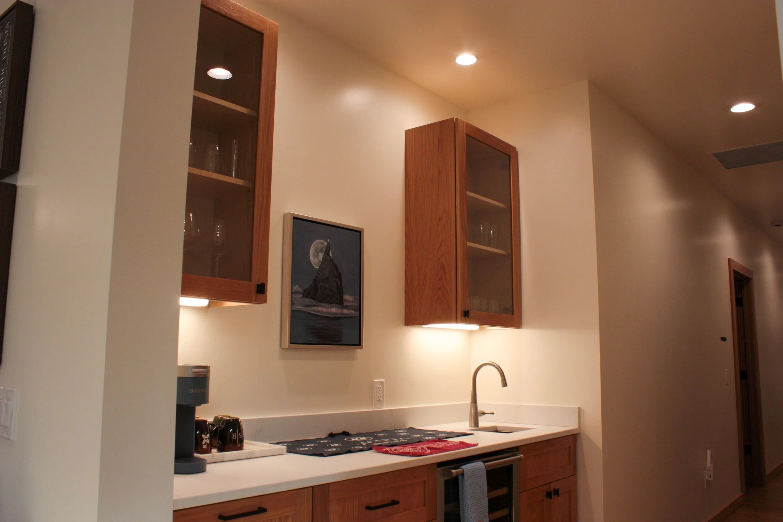 Kitchen area with wooden cabinets, a sink, a framed picture of a mountain and moon, and overhead lighting.