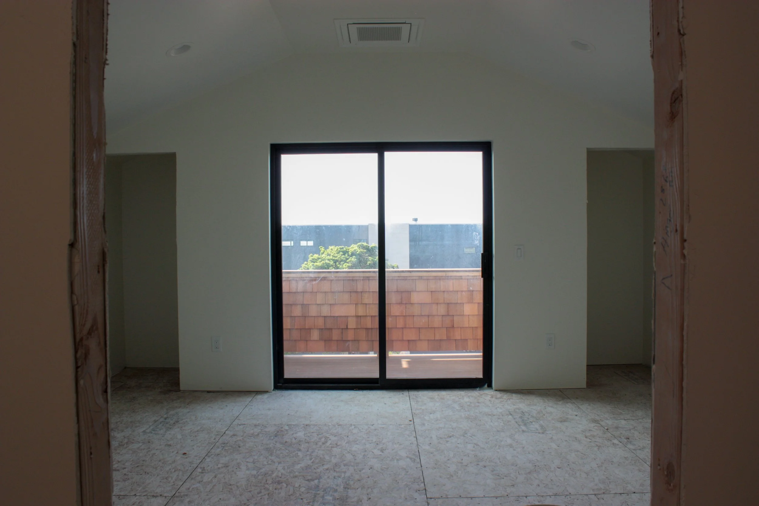 Empty room under construction with a sliding glass door leading to a balcony, framed by unfinished walls.
